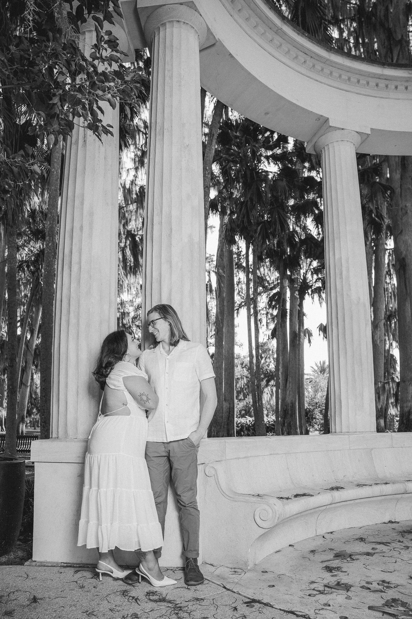 Black and white photo of couple sharing a romantic moment beside grand white columns.