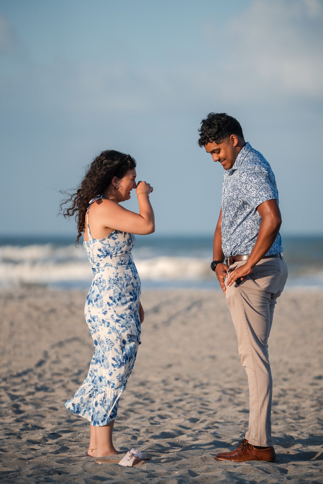 Couple laughing and enjoying a romantic moment together on a sandy beach with ocean waves in the background.
