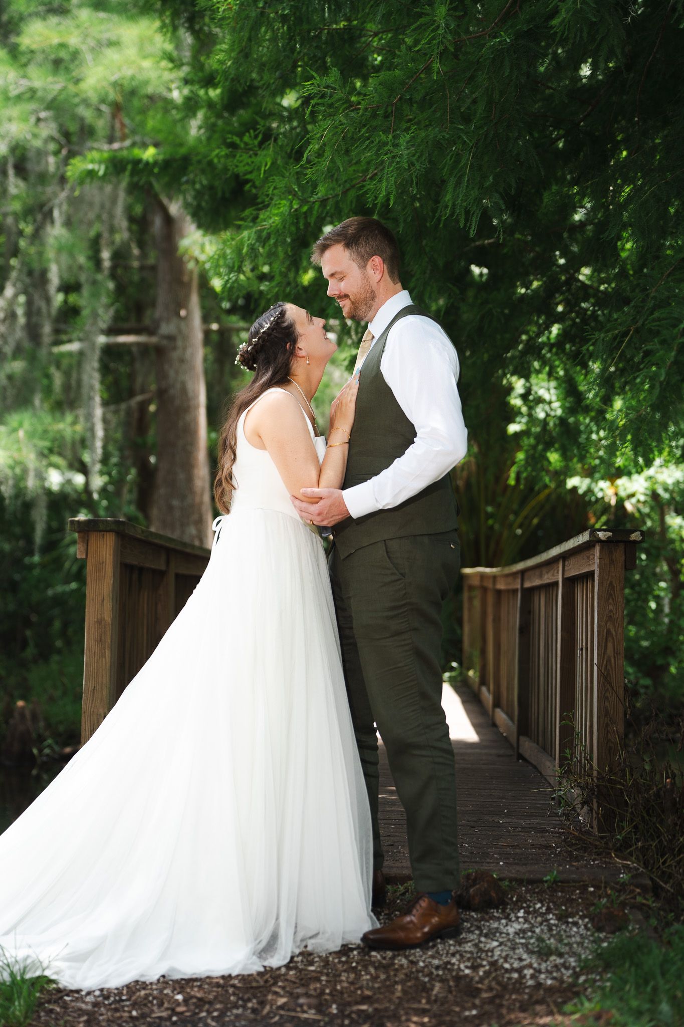 Bride and groom share romantic moment on wooden bridge in lush forest setting.