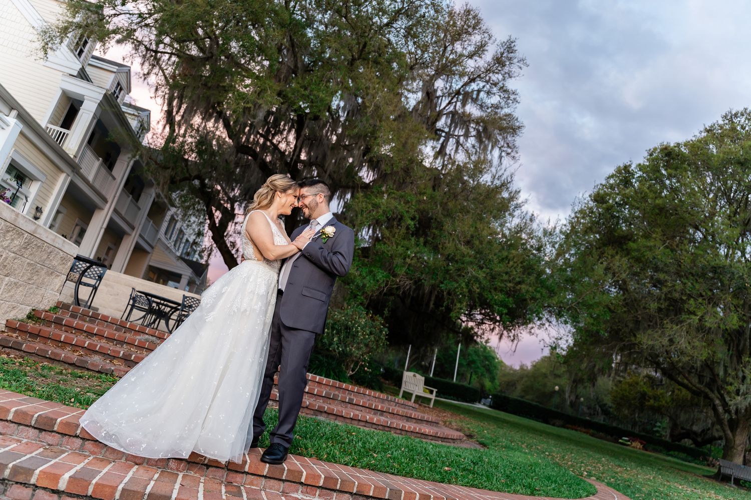 Bride and groom sharing romantic kiss on brick steps at sunset outside elegant wedding venue.