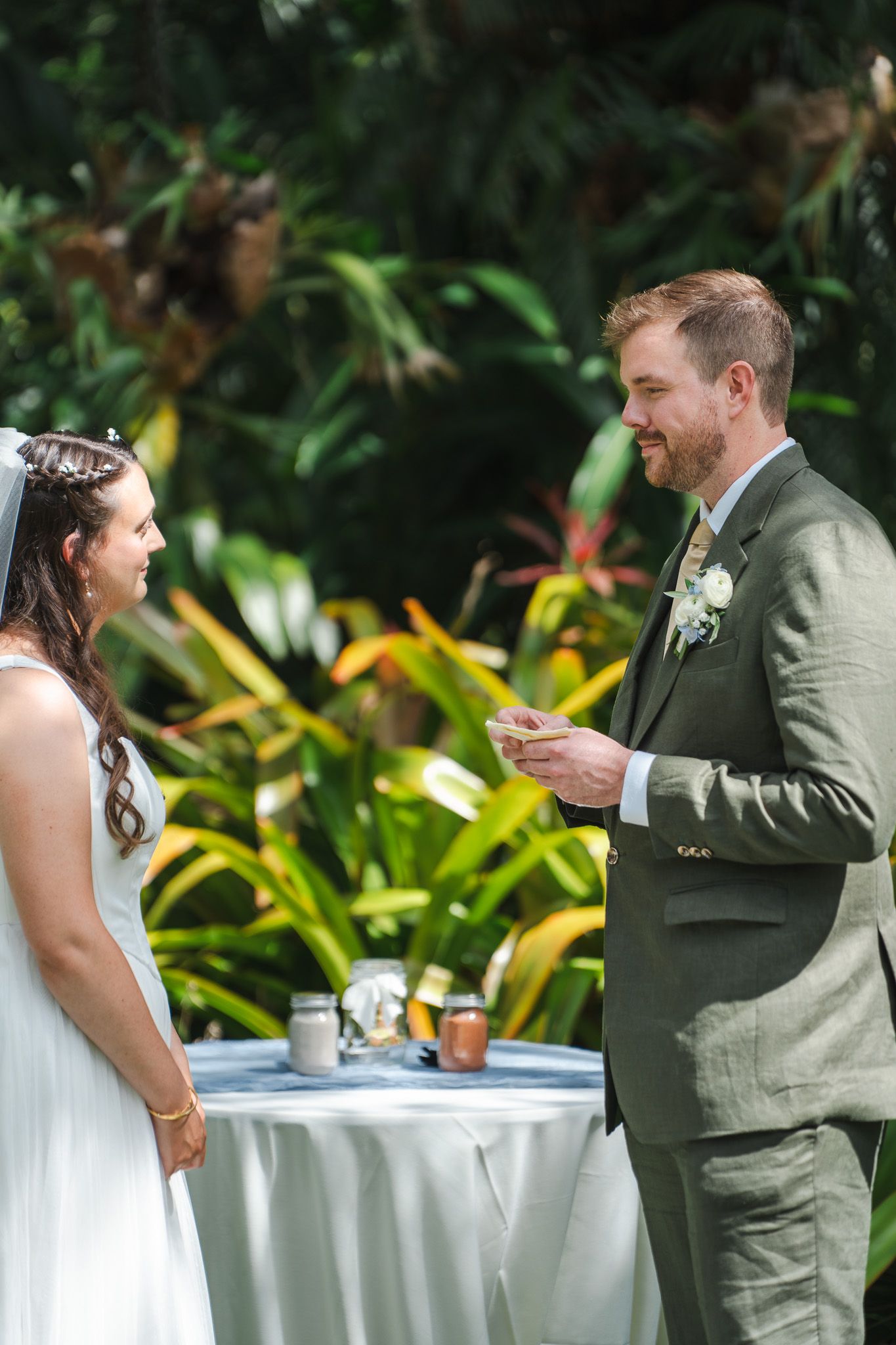 Groom reads heartfelt vows to smiling bride at elegant outdoor garden wedding ceremony.