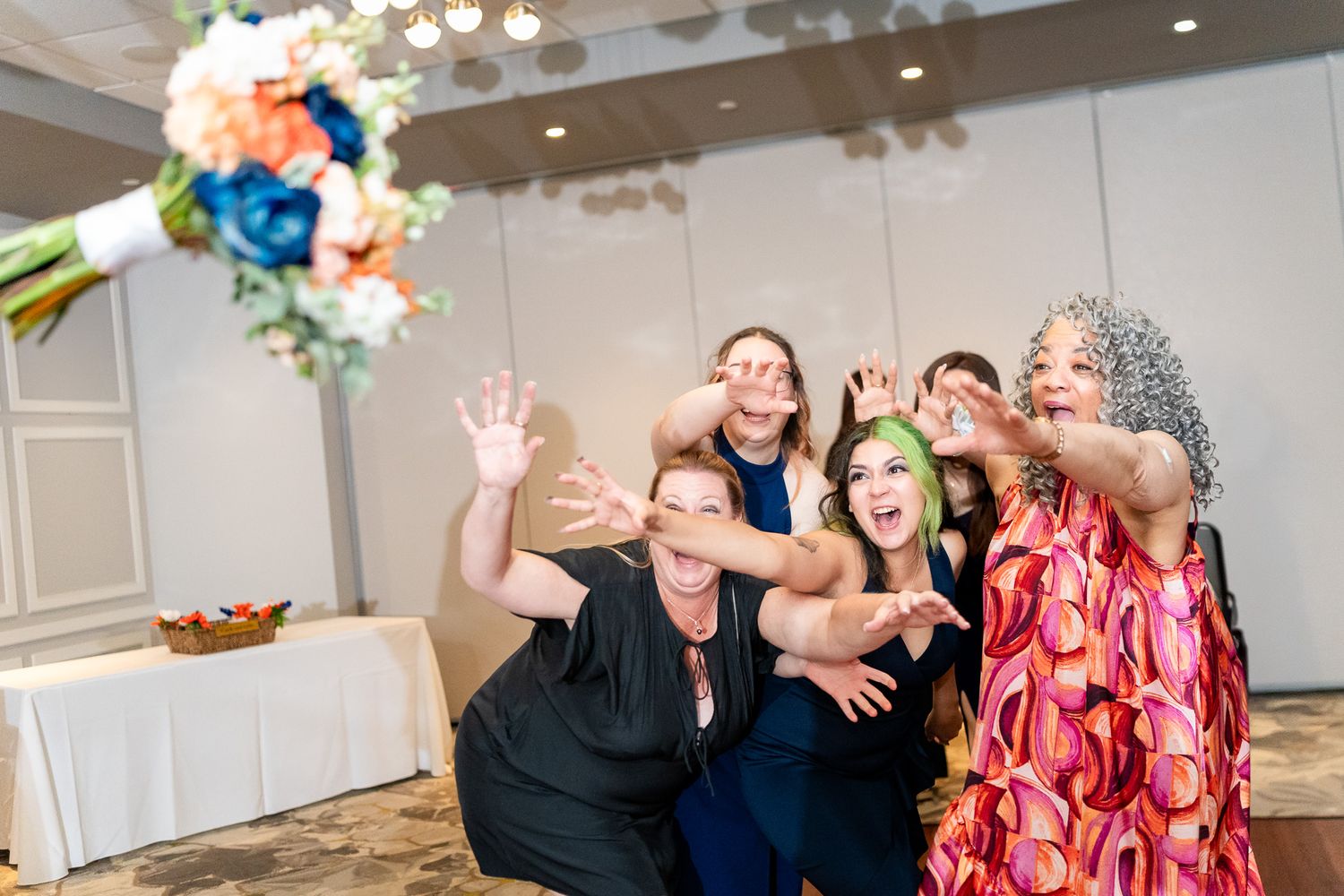 Wedding guests reach up excitedly to catch the bridal bouquet toss at the reception.
