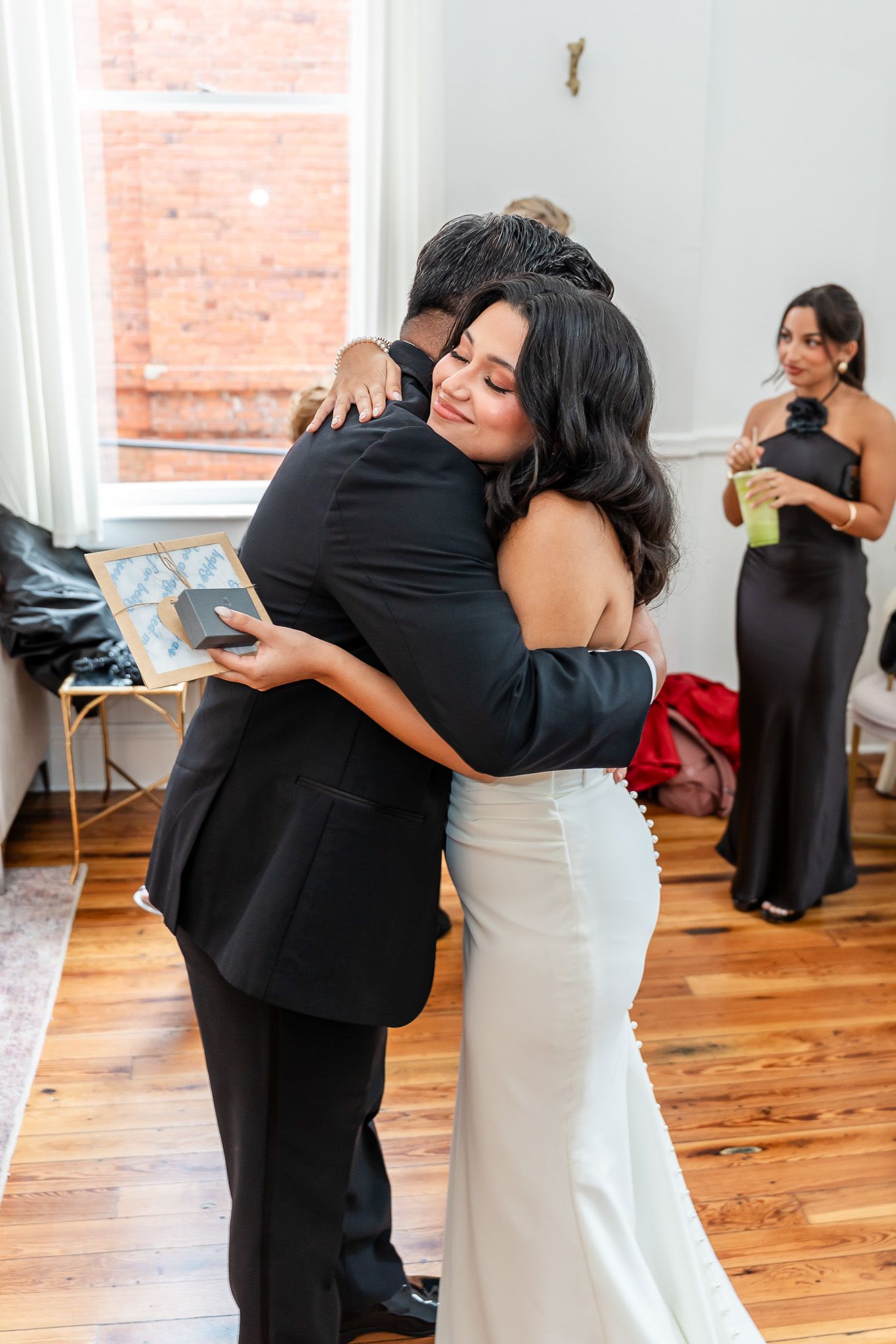 Bride in white gown hugging guest while holding framed photo at wedding.