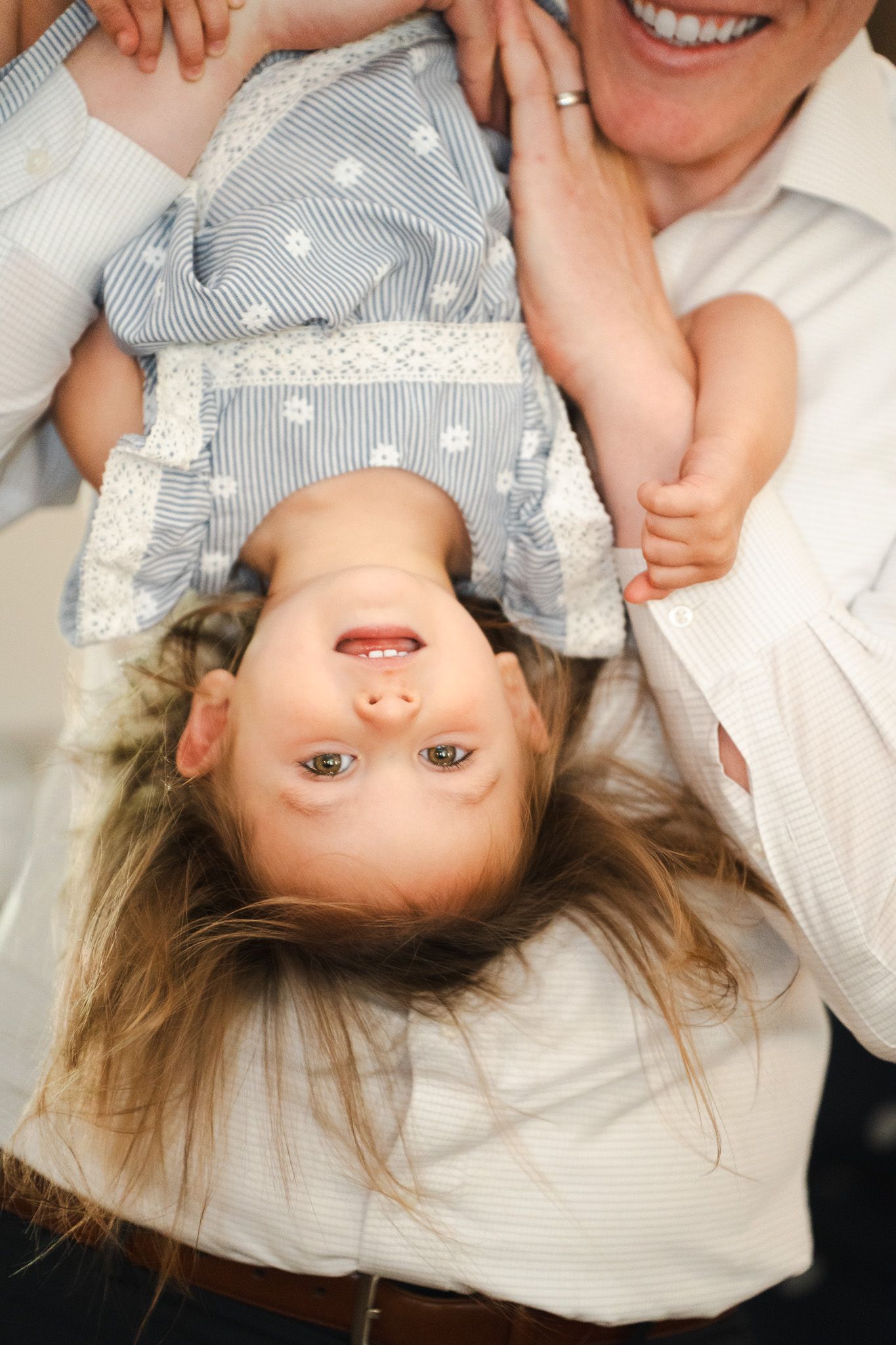 Laughing adult holds giggling young child upside down in playful moment.