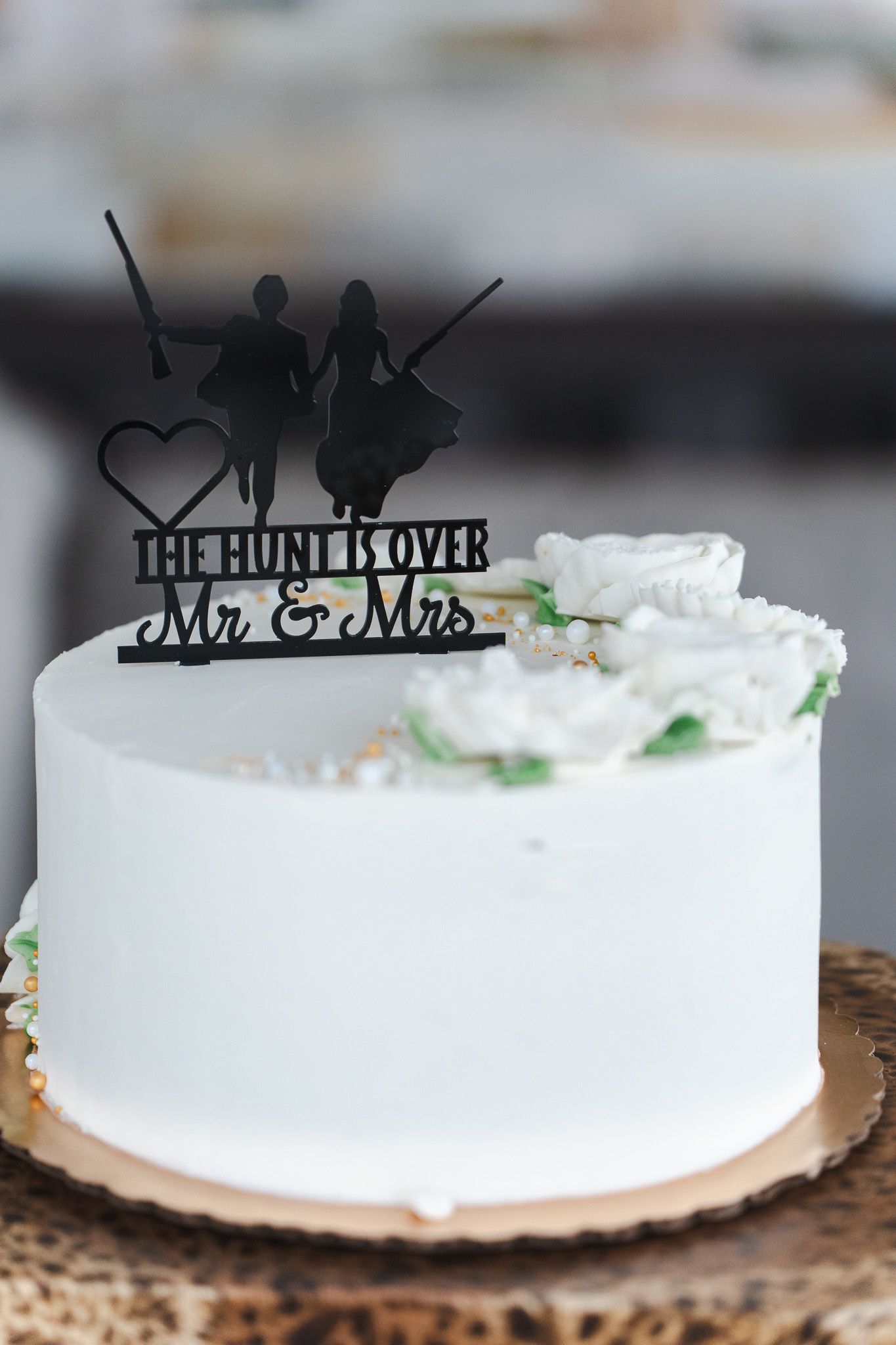 White wedding cake with black silhouette topper reading The Hunt Is Over Mr and Mrs.