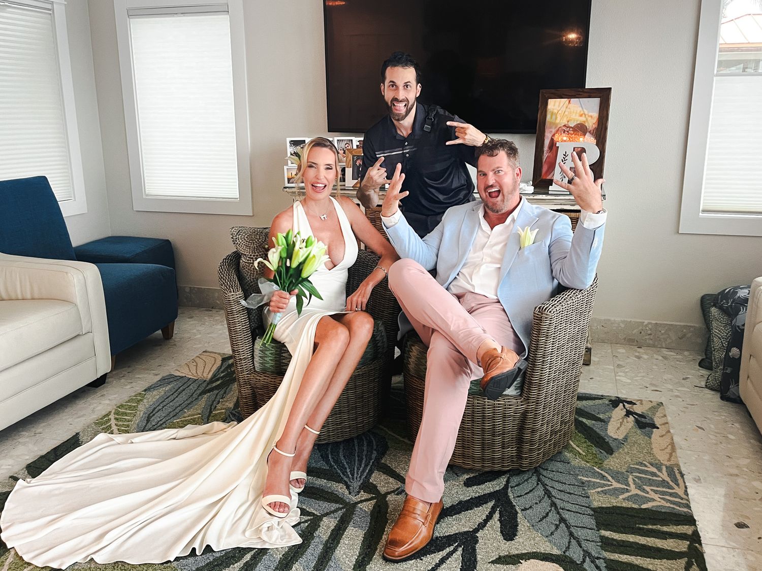Bride and groom laughing with their photographer in a beachside vacation rental before the wedding.