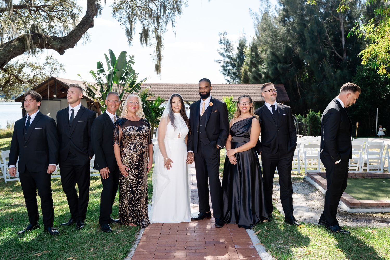Wedding party of eight poses in formal attire on brick path beneath Spanish moss-draped oak trees.