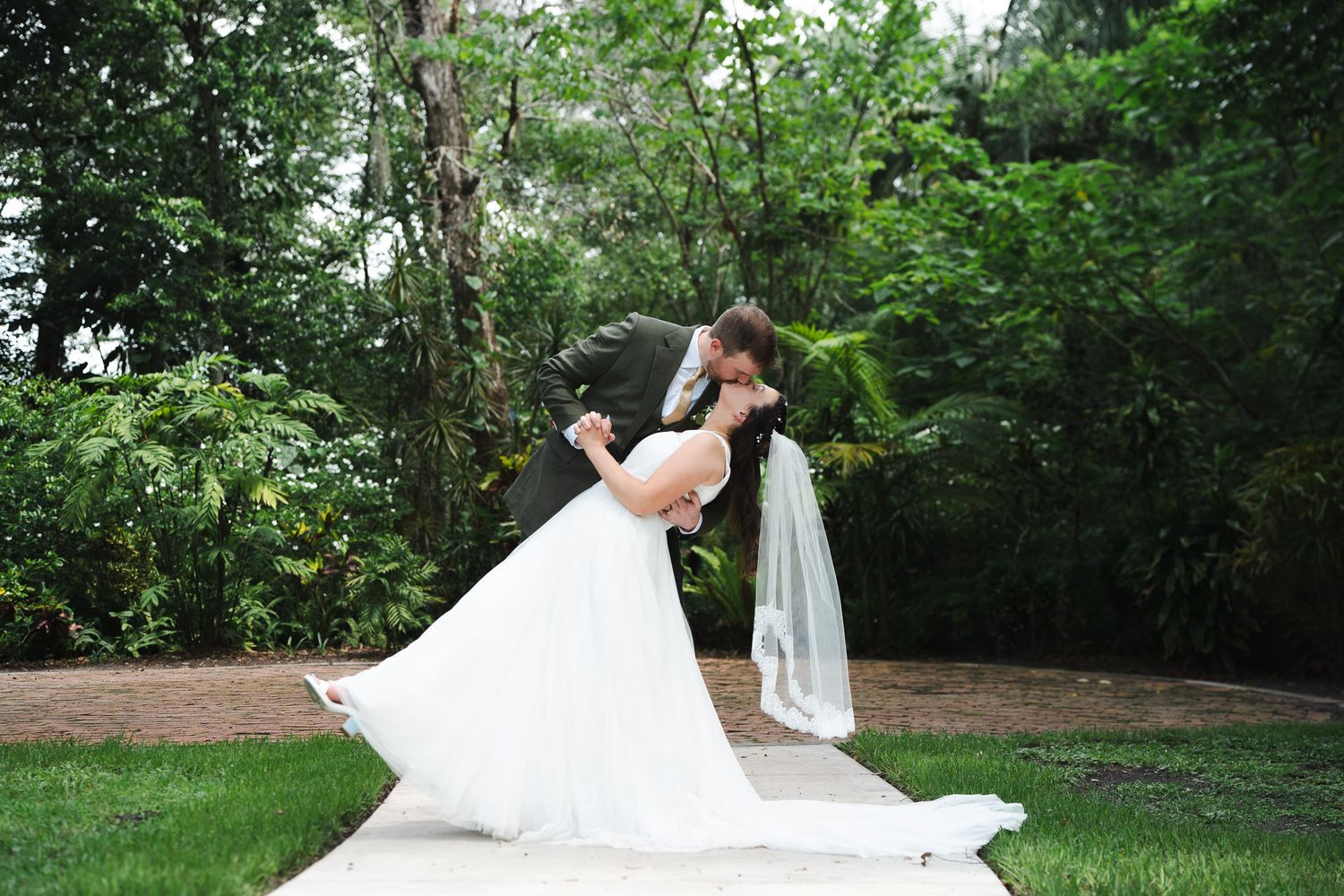 Groom dips bride for a romantic kiss outdoors during their garden wedding portrait session.
