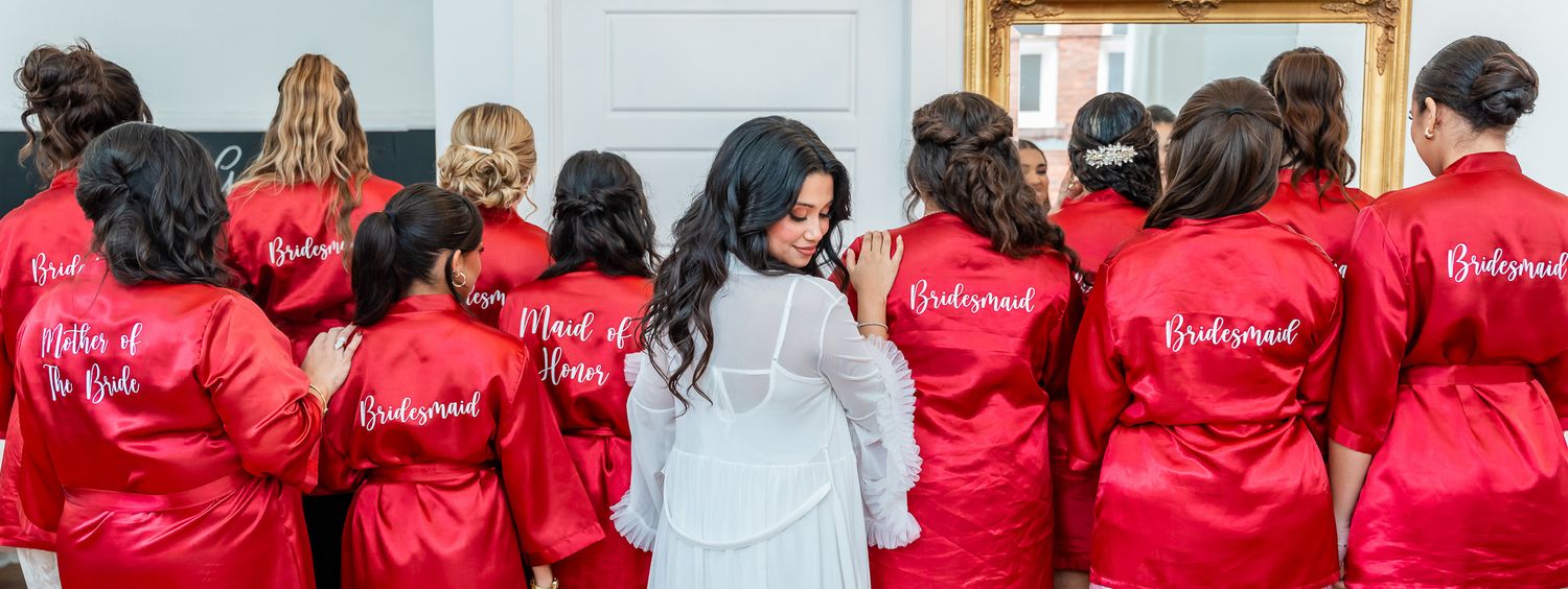 Bridesmaids in matching red satin robes with personalized text stand together showing their backs.