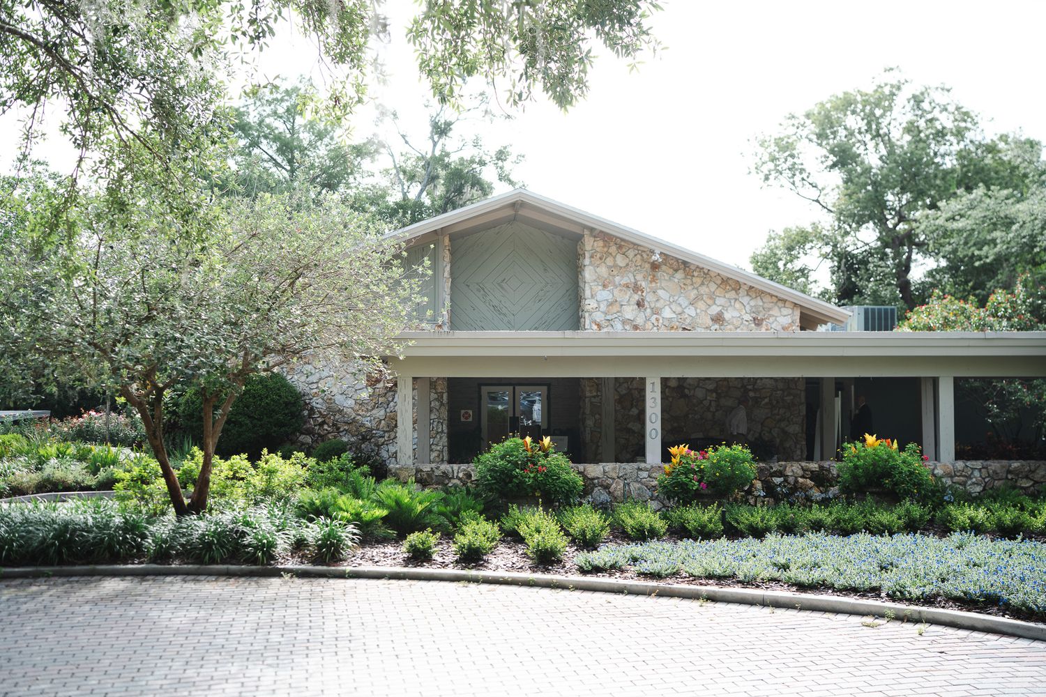 Stone and wood mid-century modern wedding venue exterior surrounded by mature trees and landscaping.