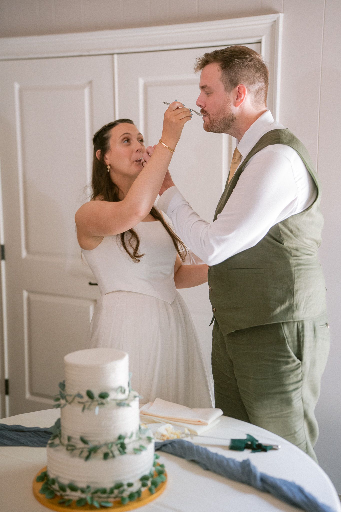 Bride and groom feed each other wedding cake at white three-tier decorated reception.