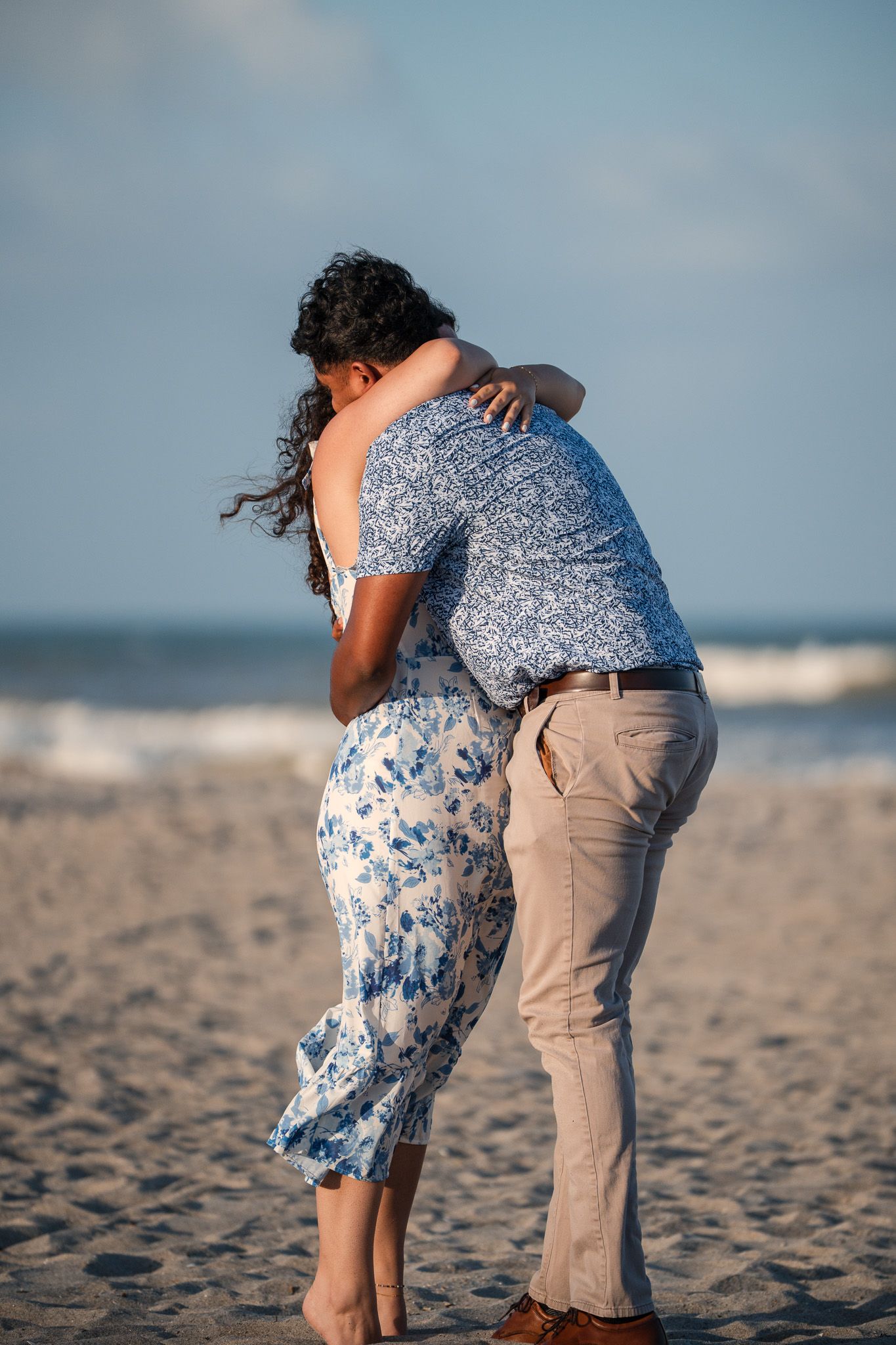 Couple sharing a romantic embrace on a sandy beach with ocean waves in the background.