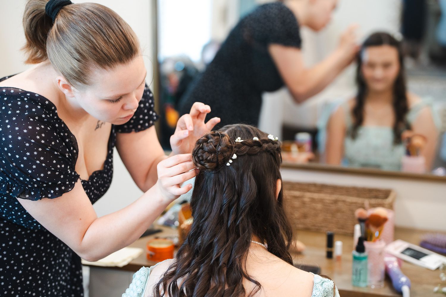 Hair stylist carefully braiding and pinning bride's dark hair with pearl accessories.
