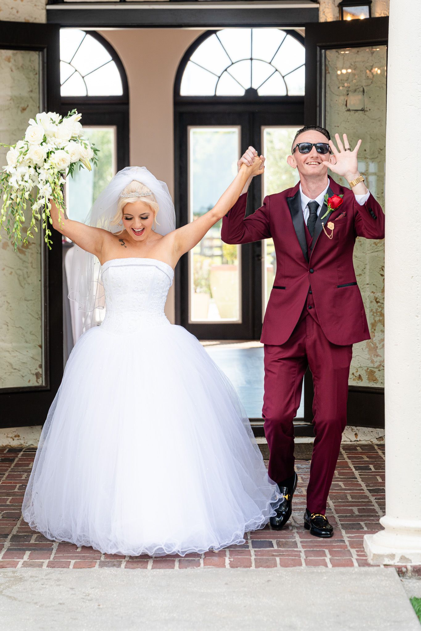 Joyful bride in white ball gown and groom in burgundy suit celebrating their wedding exit.
