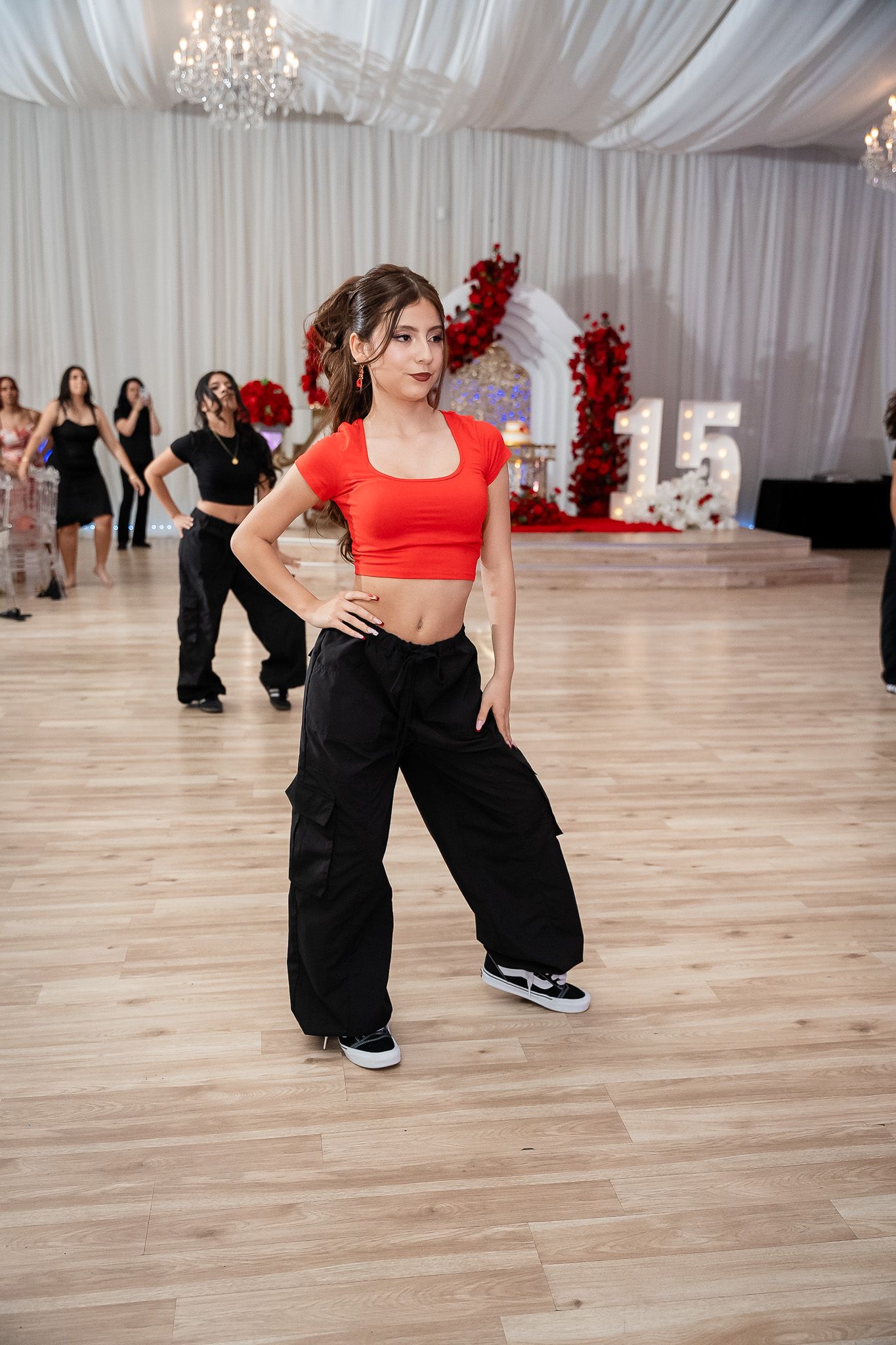 Teen girl in red crop top and black cargo pants dances at quinceañera sweet 15 party venue.