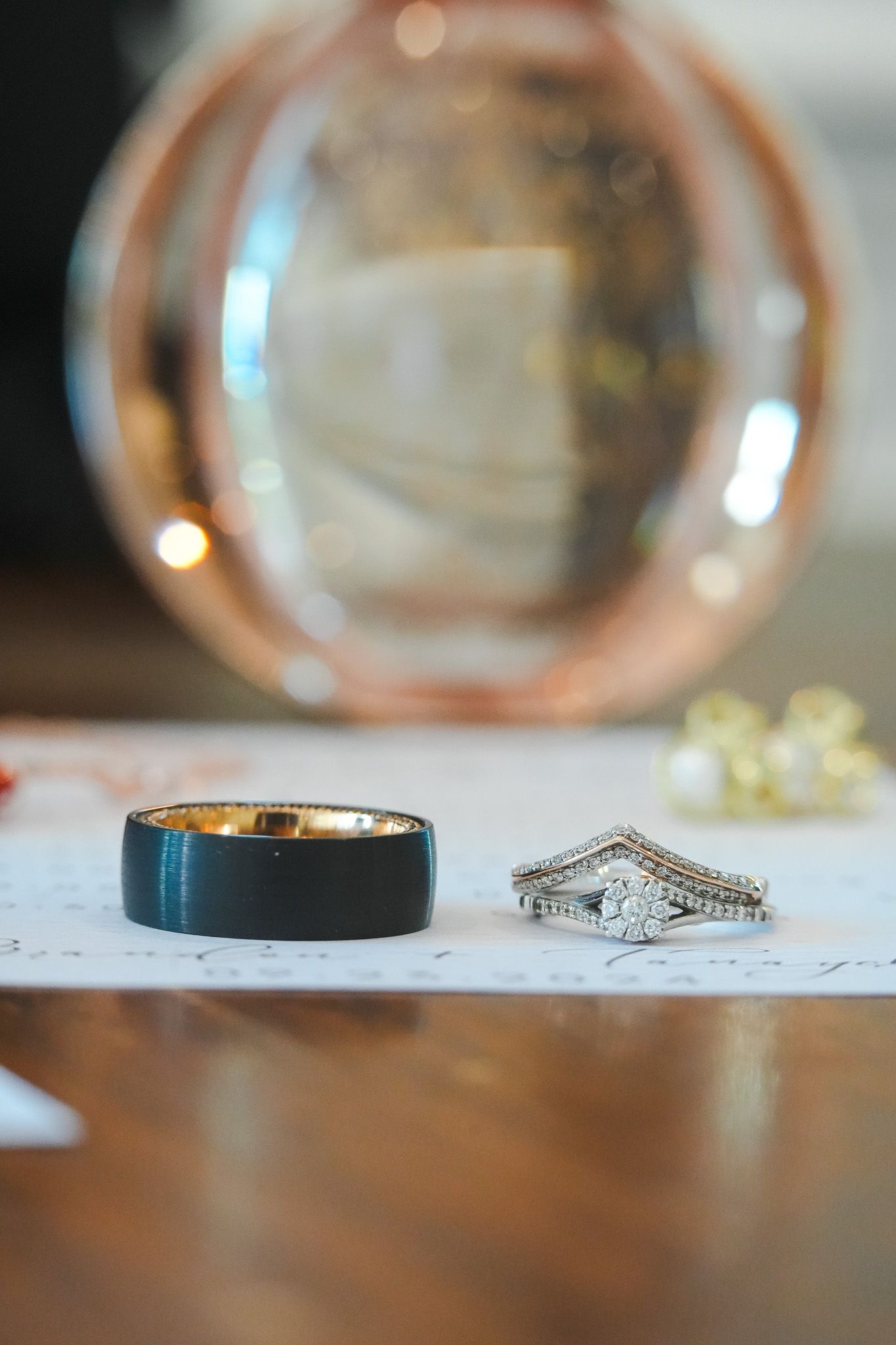 Wedding rings displayed on paper, featuring a black tungsten band and diamond engagement ring set with chevron band.