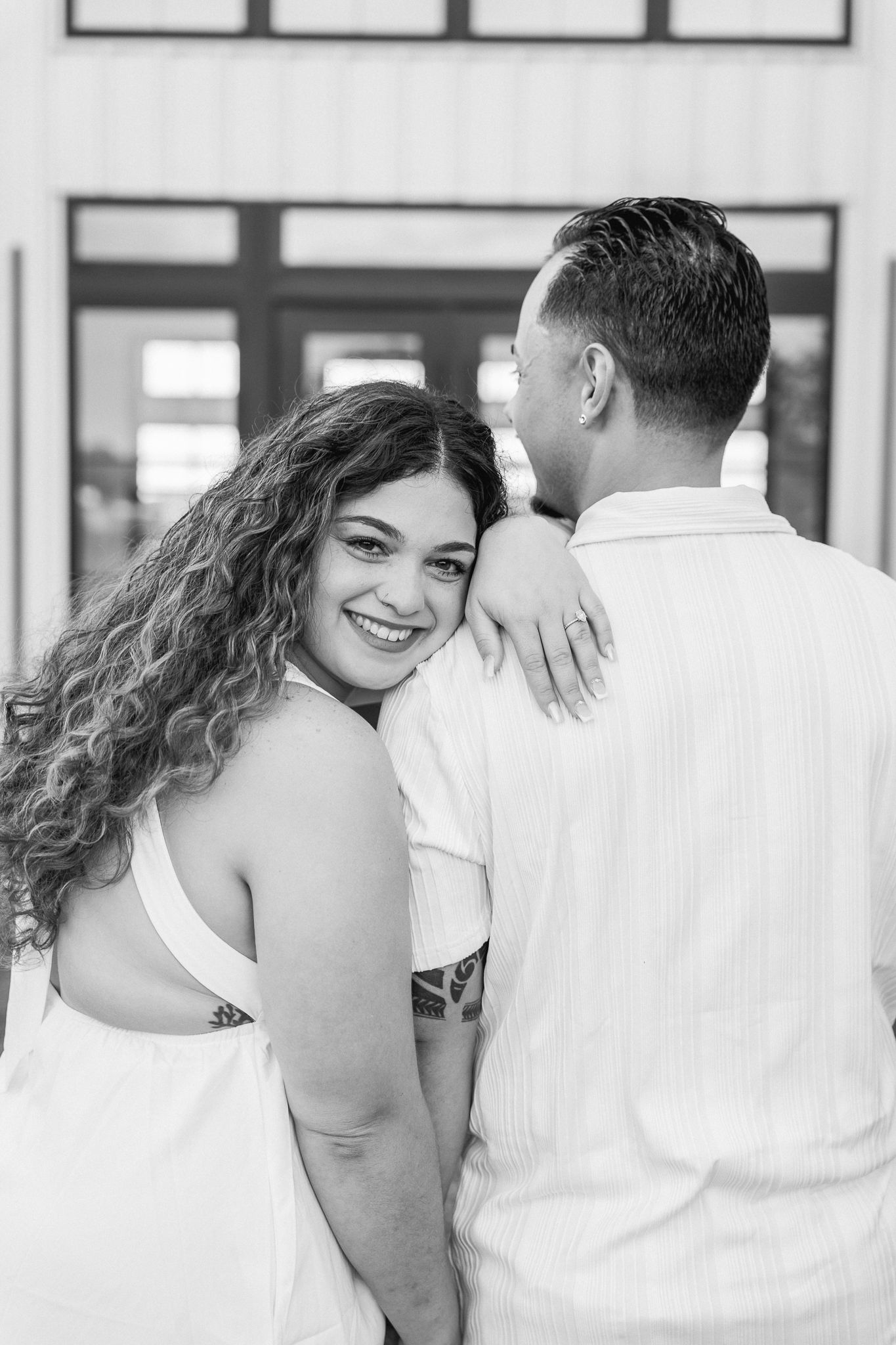 Black and white photo of smiling woman leaning on mans shoulder outdoors.