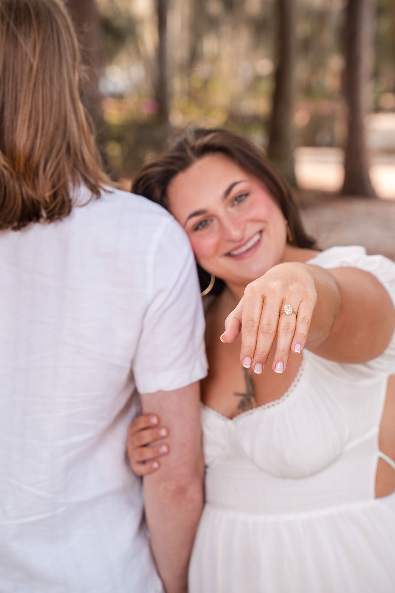 Smiling woman showing off her engagement ring while embracing her partner outdoors.