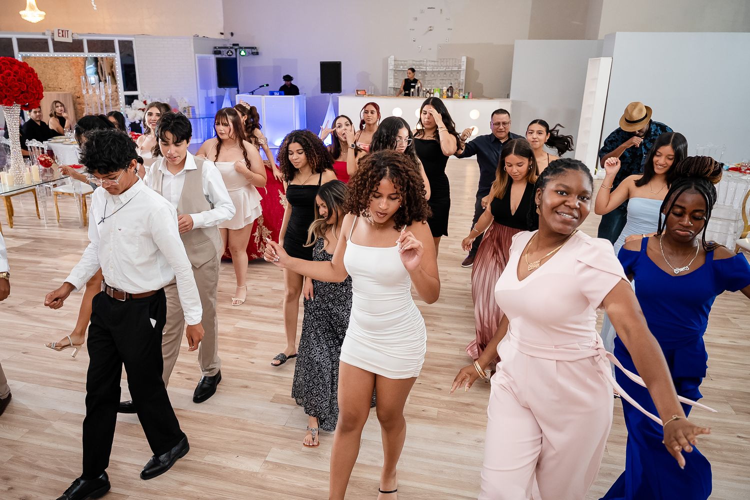 Diverse group of guests dancing joyfully at an elegant indoor quinceañera reception party.