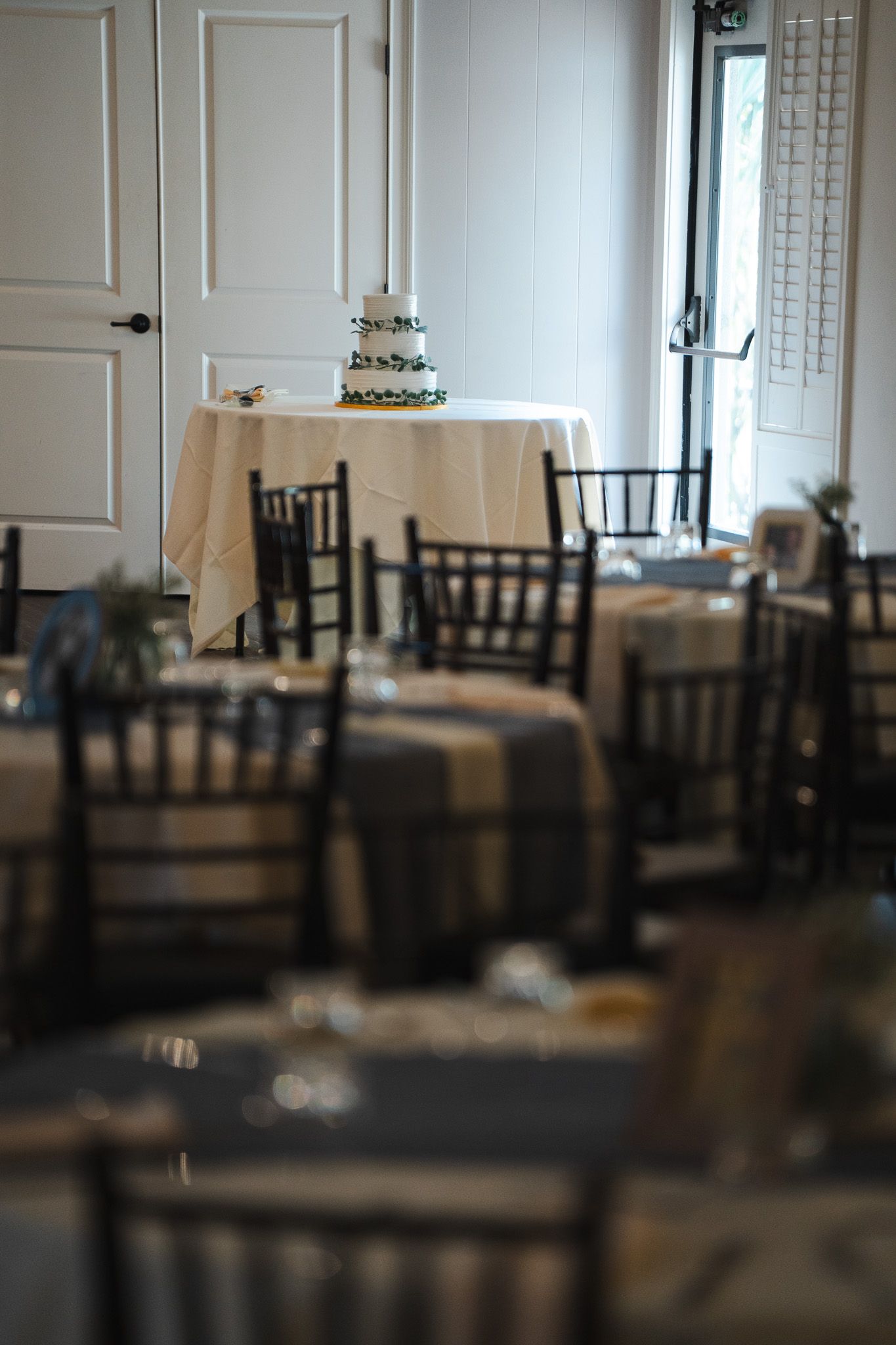 Elegant wedding reception hall with chiavari chairs and a tiered cake on a draped table.
