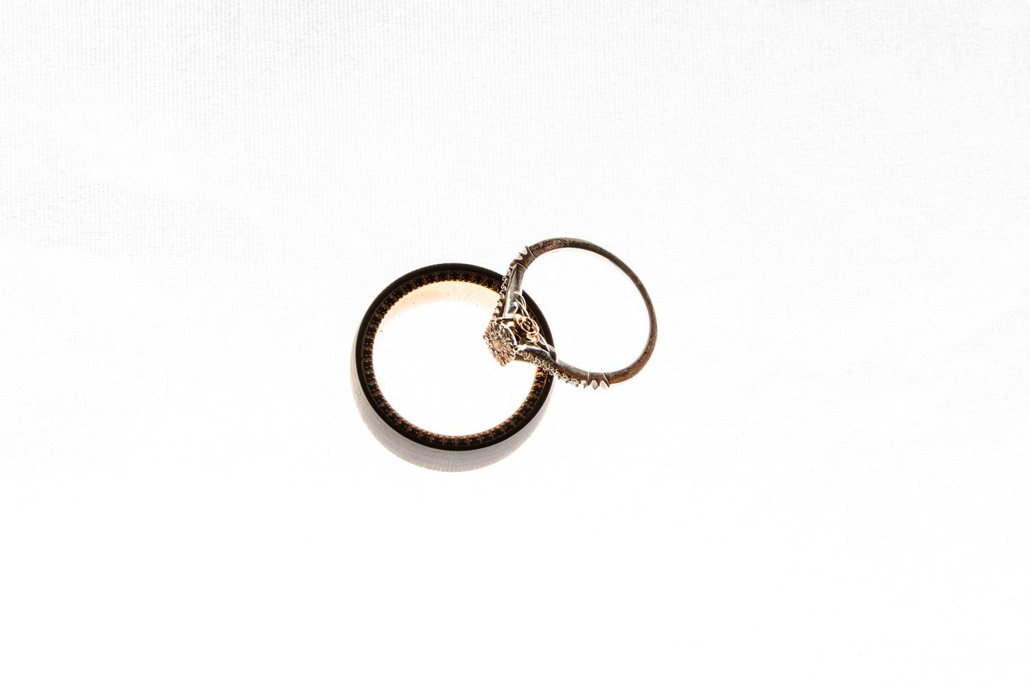 Two interlinked wedding rings, a plain gold band and a diamond solitaire engagement ring, on white background.