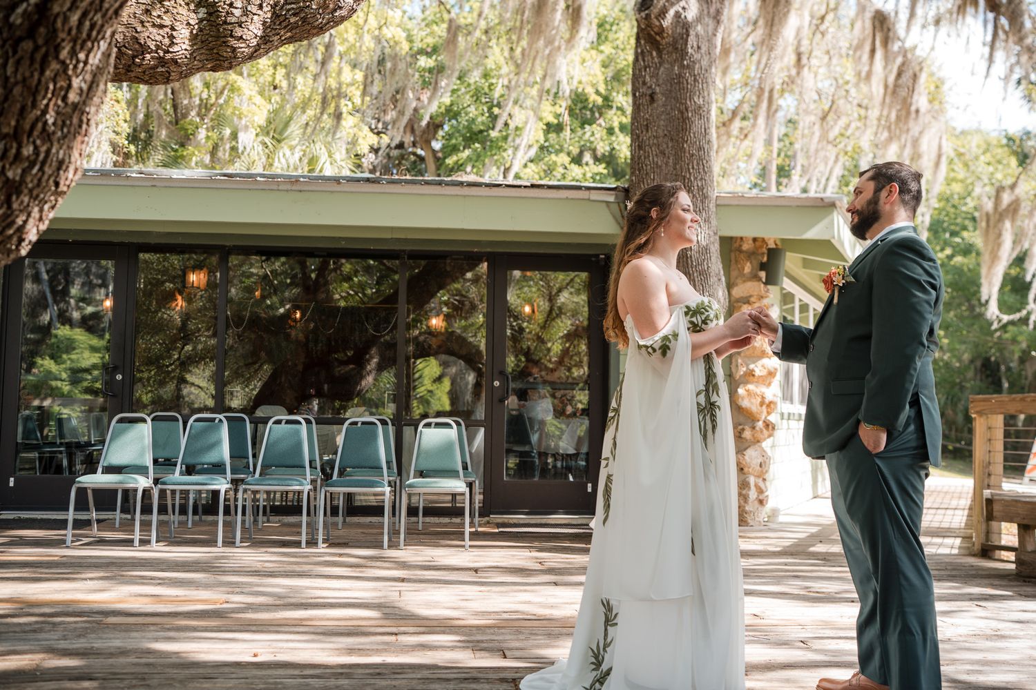 Bride and groom share first look moment outdoors near rustic venue surrounded by moss-draped trees.
