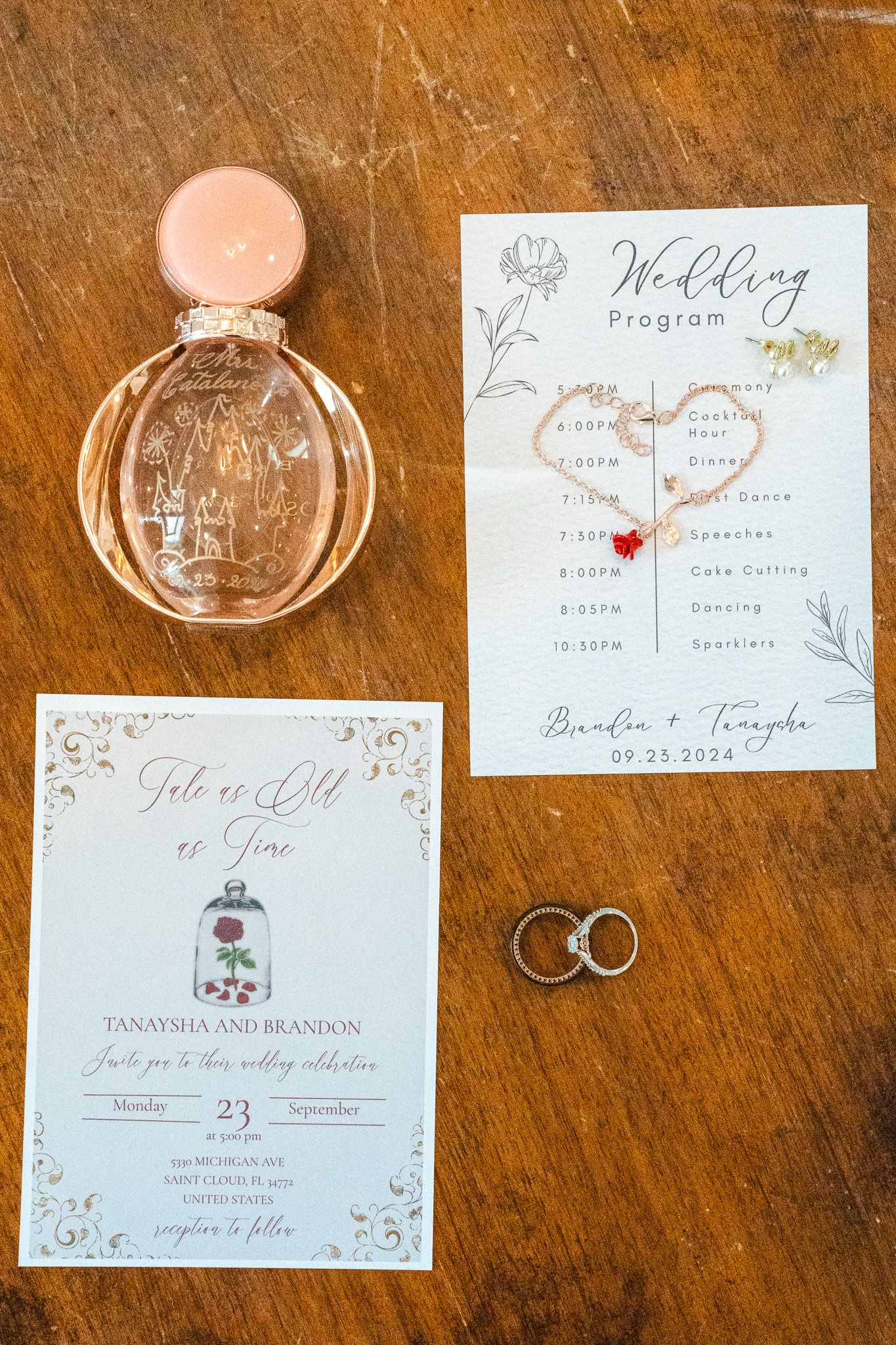 Beauty and the Beast themed wedding stationery with rings, perfume bottle, and program on wooden table.