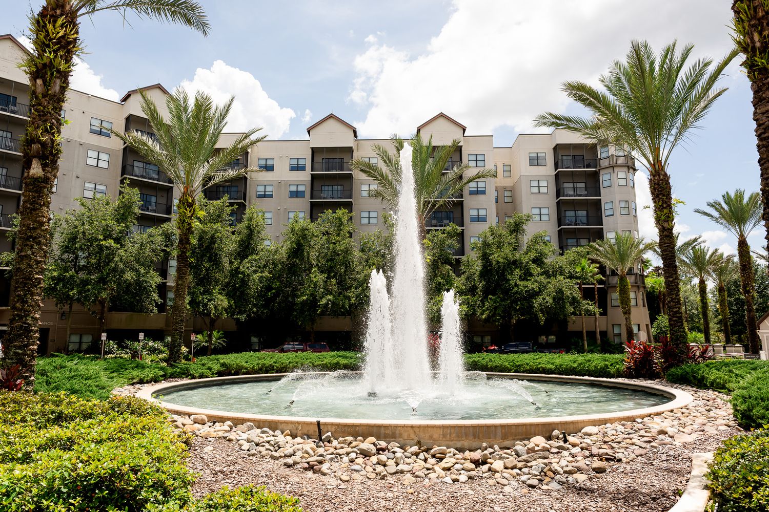 Elegant fountain surrounded by palm trees in front of a multi-story resort building.