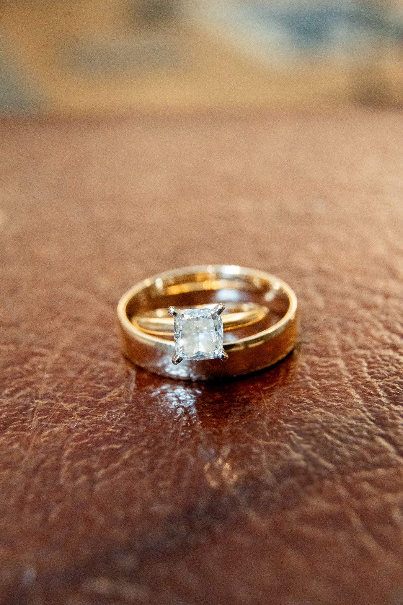 Gold wedding band set with square diamond solitaire engagement ring on brown leather surface.