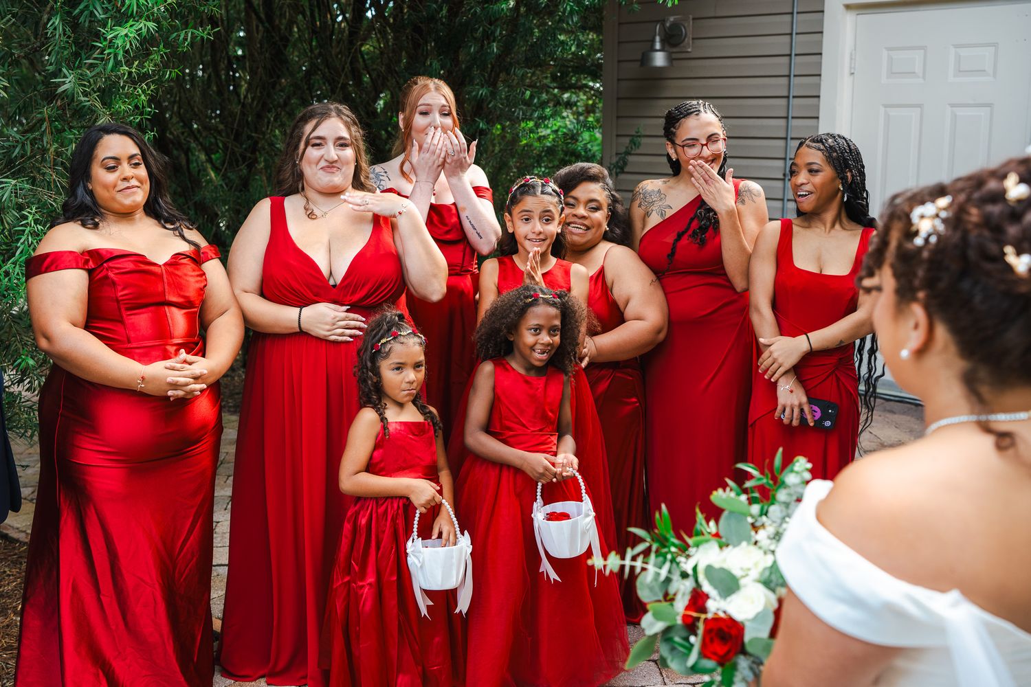 Bridesmaids in red dresses react emotionally seeing bride for first time on wedding day.