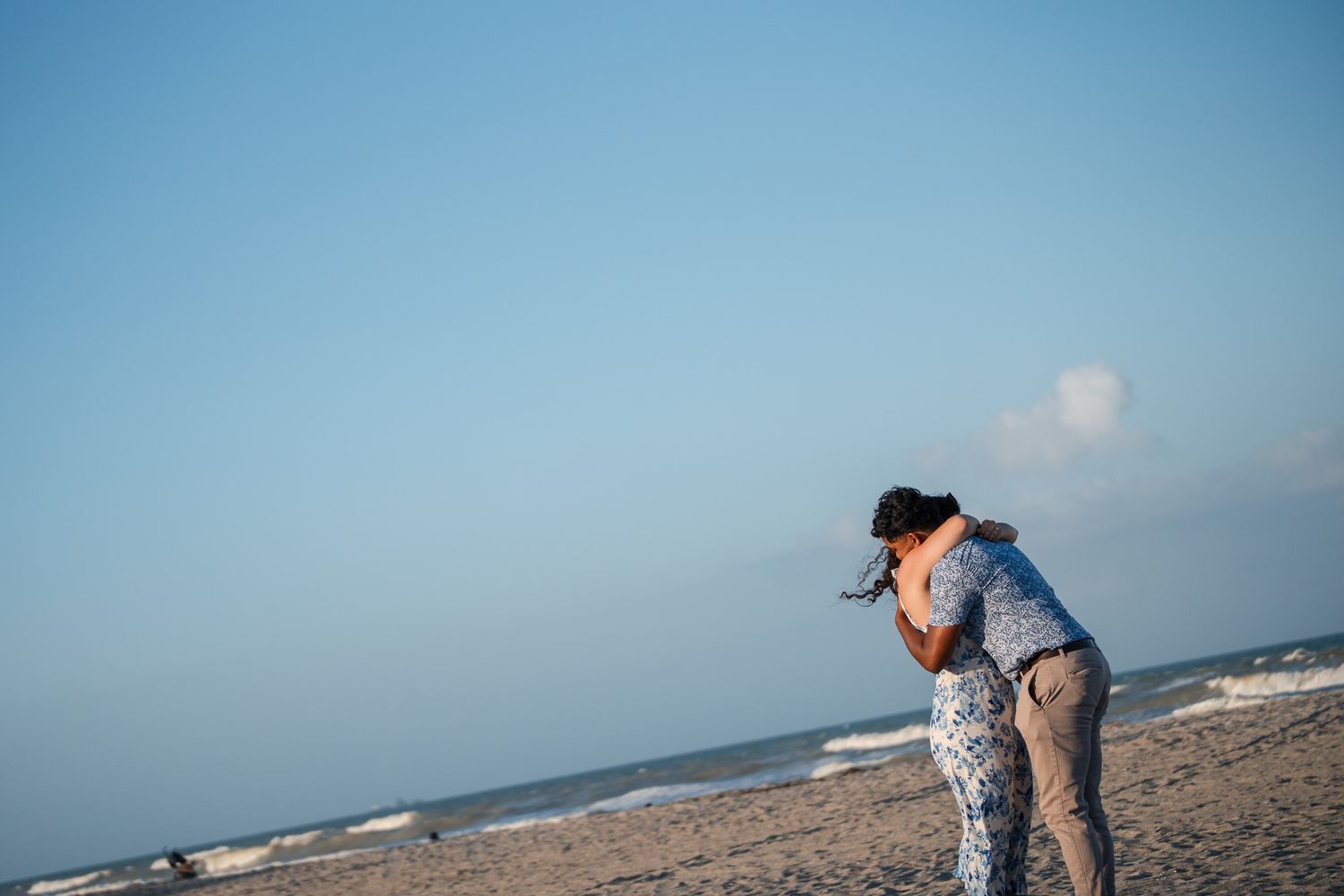 Couple shares a romantic embrace on a serene beach with gentle ocean waves in the background.