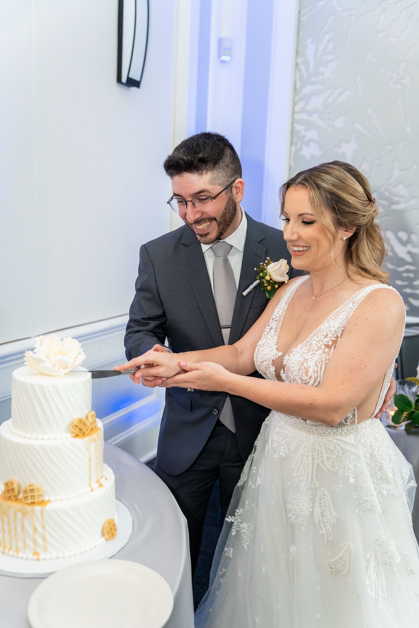 Smiling bride and groom cut their elegant three-tier white and gold wedding cake together.