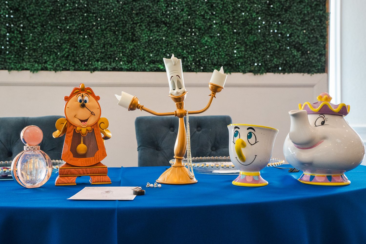 Beauty and the Beast character figurines displayed on blue table with green hedge backdrop.