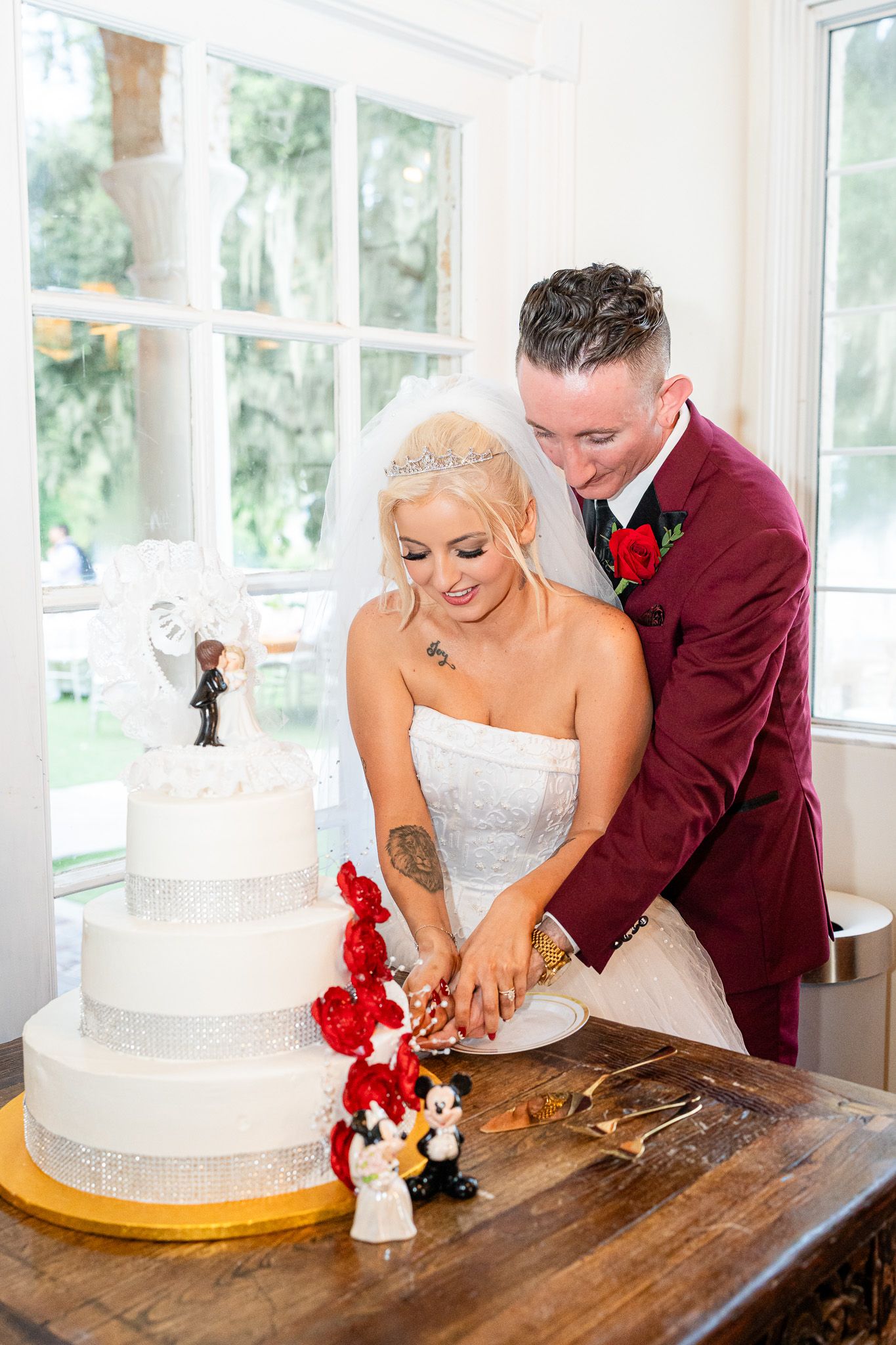 Bride and groom cutting elegant white tiered wedding cake decorated with festive figurines.