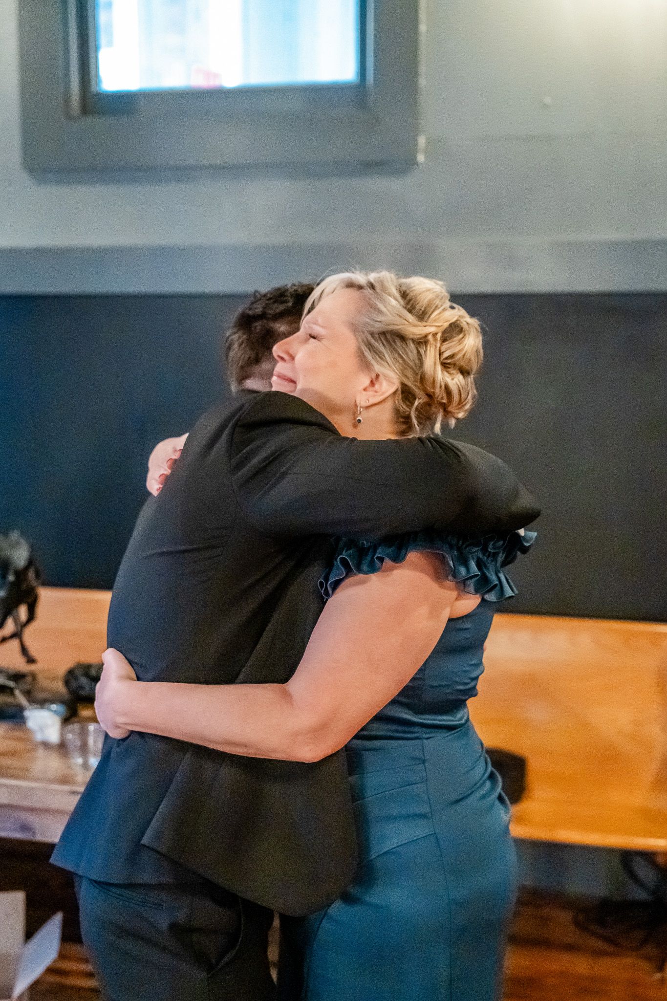 Emotional hug between two guests in formal attire at wedding reception.