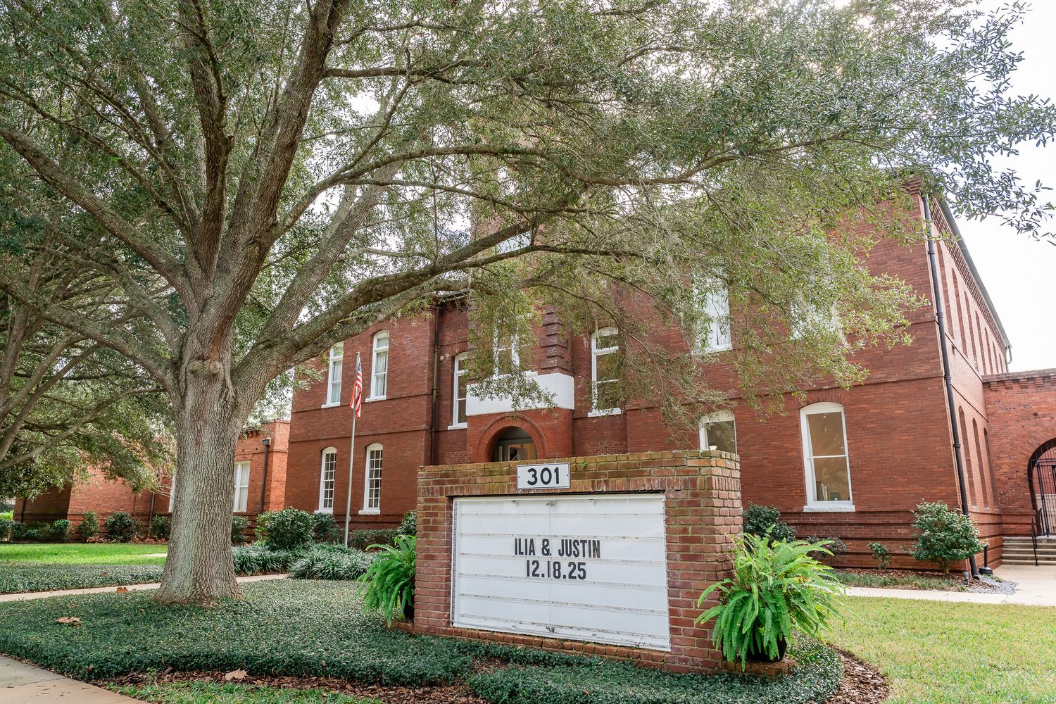 Historic red brick wedding venue with marquee sign displaying bride and groom names and date.