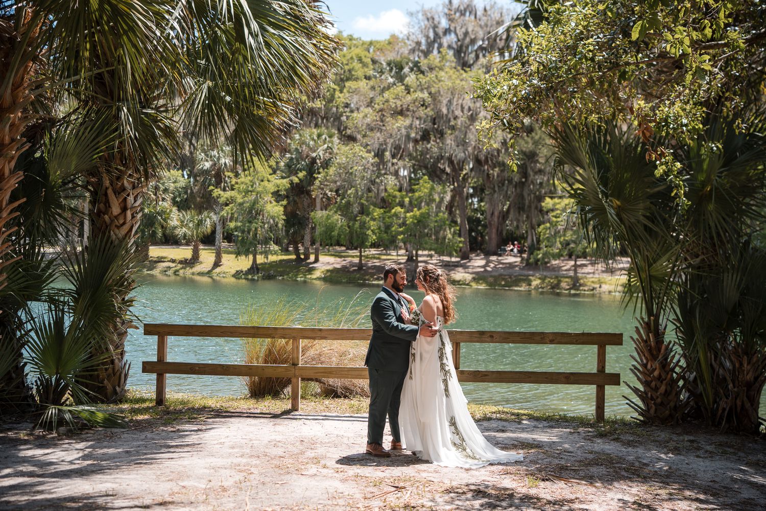 Bride and groom share vows with officiant by turquoise lake surrounded by palm trees in Florida.
