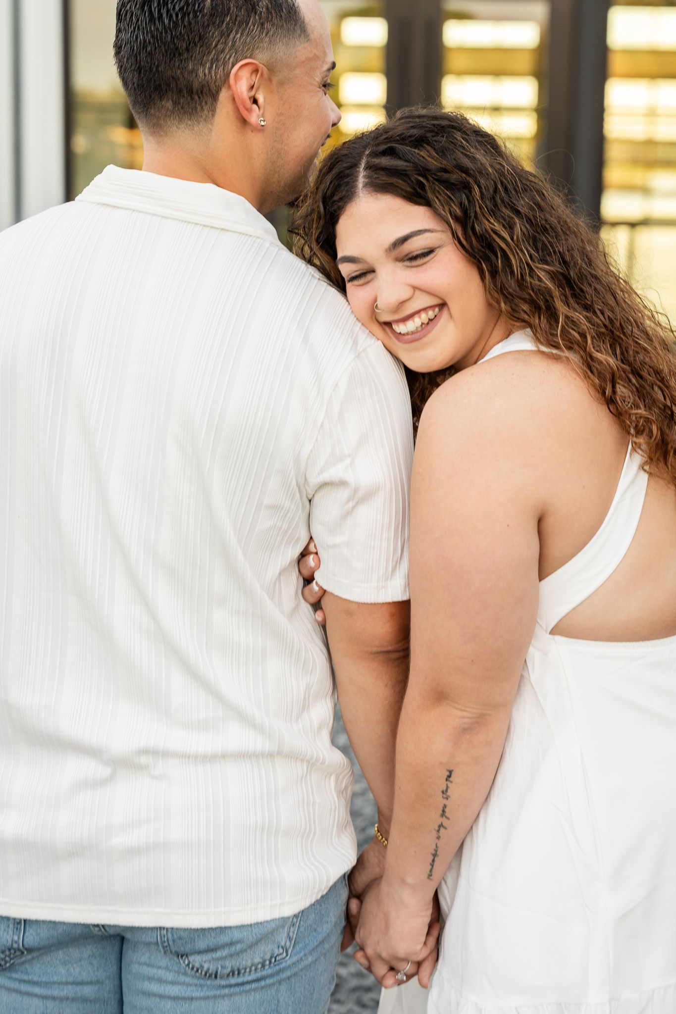 Happy woman smiling while leaning against her partner, holding hands during an outdoor couples session.