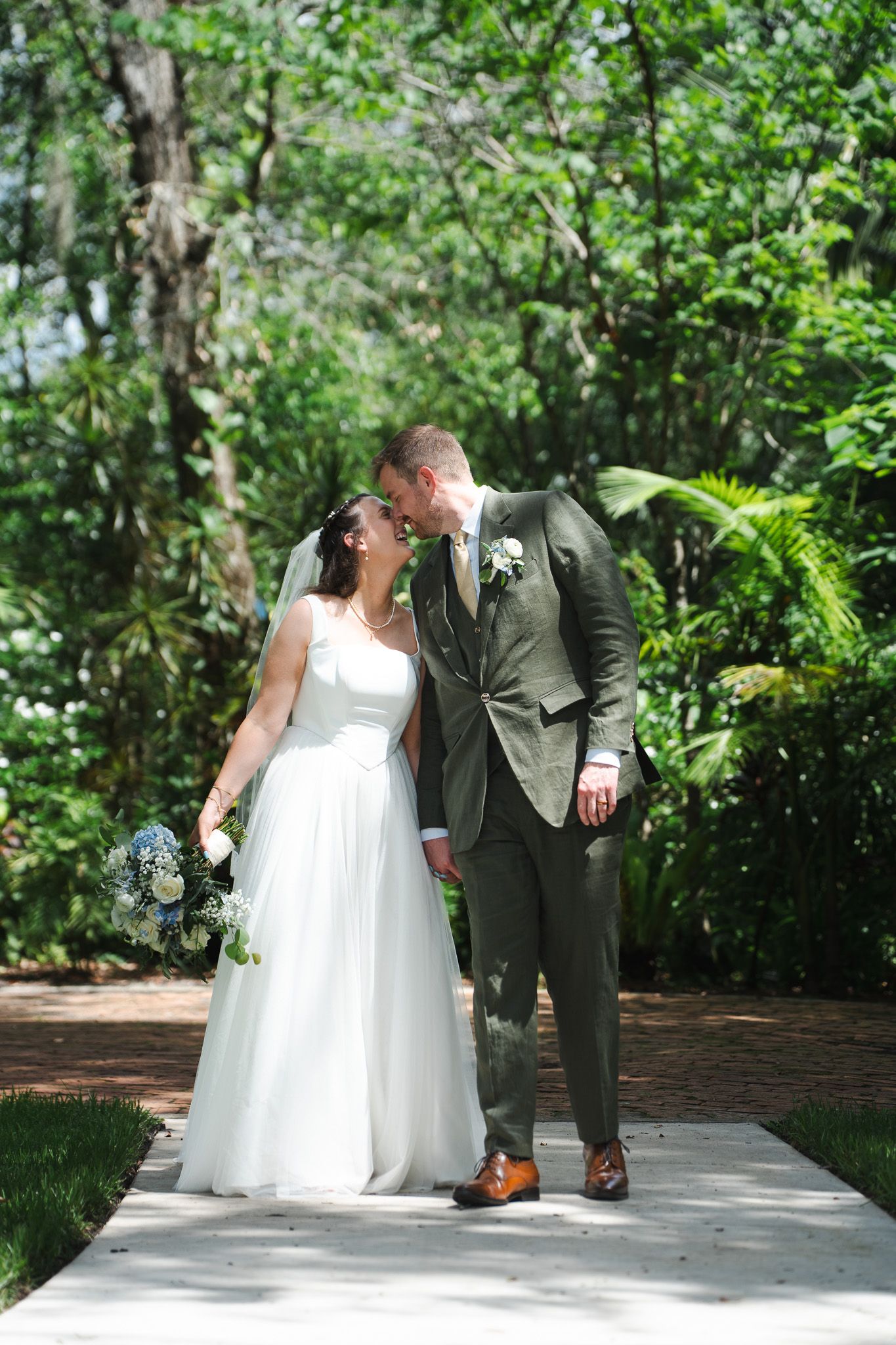 Bride and groom share a romantic kiss while walking along a garden pathway on their wedding day.