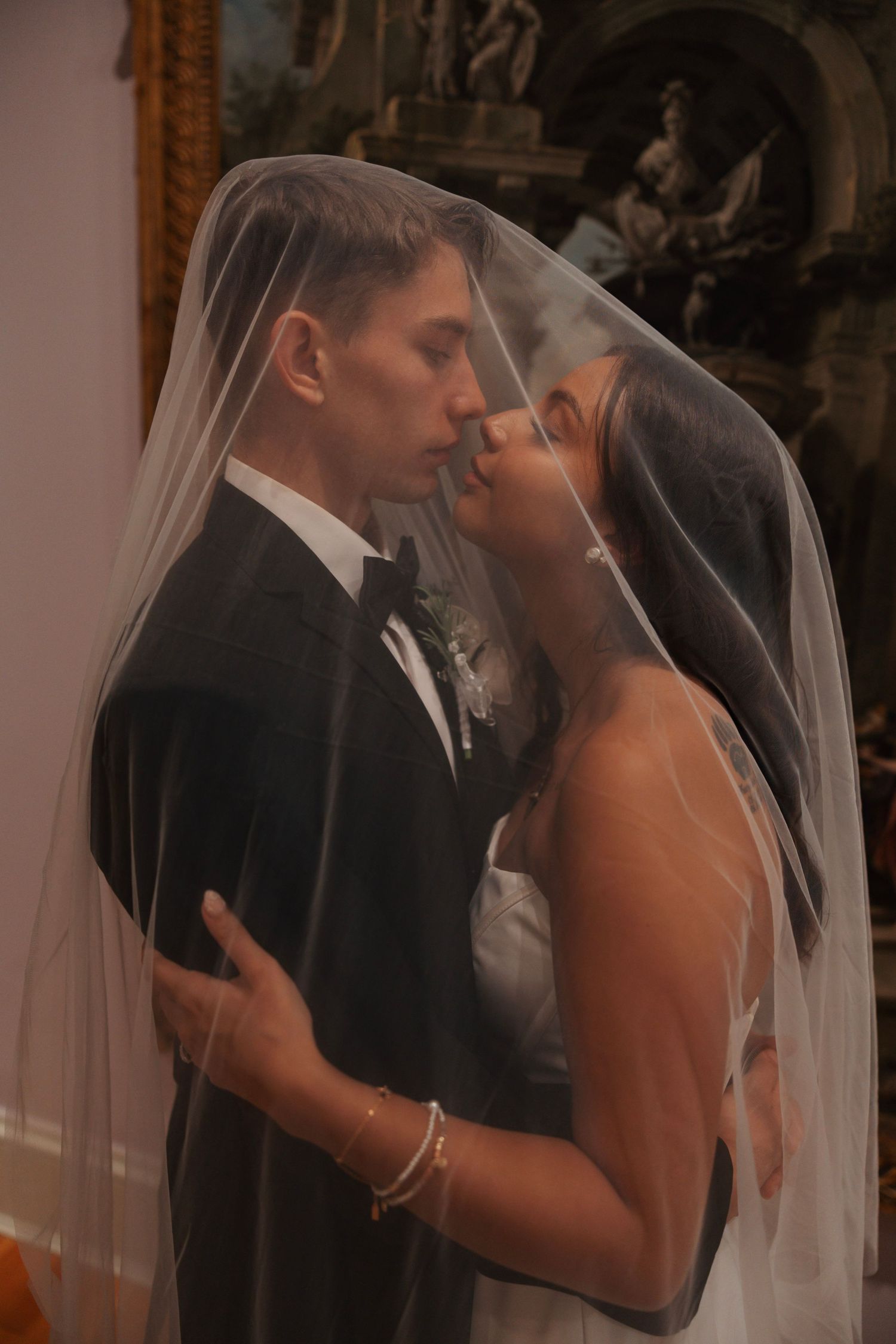 Bride and groom share a romantic kiss under a flowing white wedding veil at their elegant ceremony.