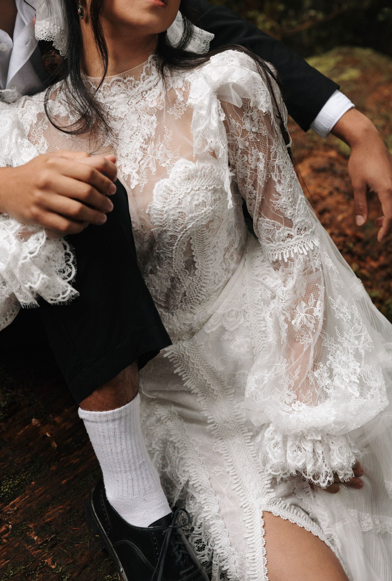 Close-up detail of bride wearing sheer lace long-sleeve wedding dress with intricate floral embroidery.