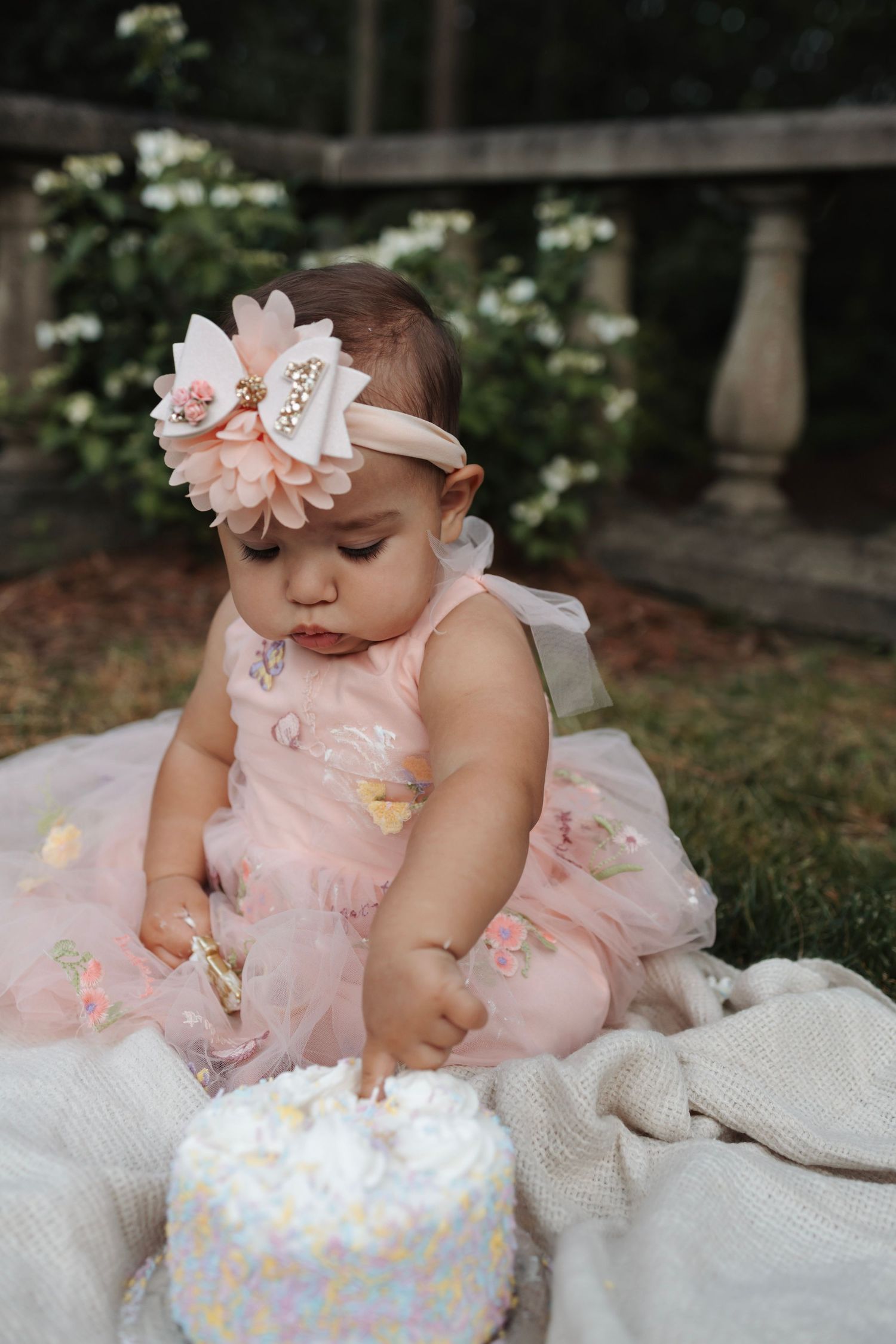 Adorable baby girl in pink tutu dress with floral headband celebrating first birthday with smash cake outdoors.