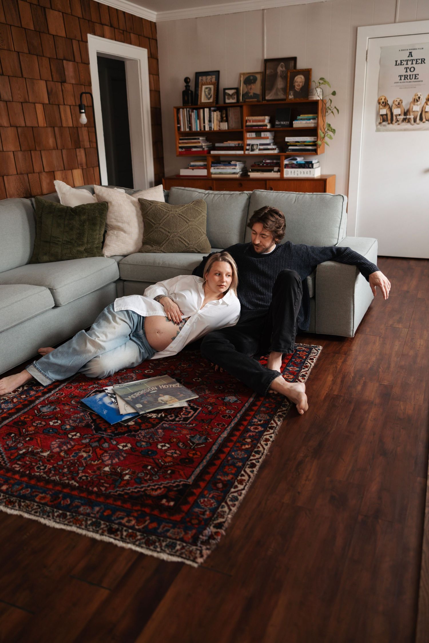 Pregnant couple relaxing together on living room floor leaning against a gray sectional sofa.