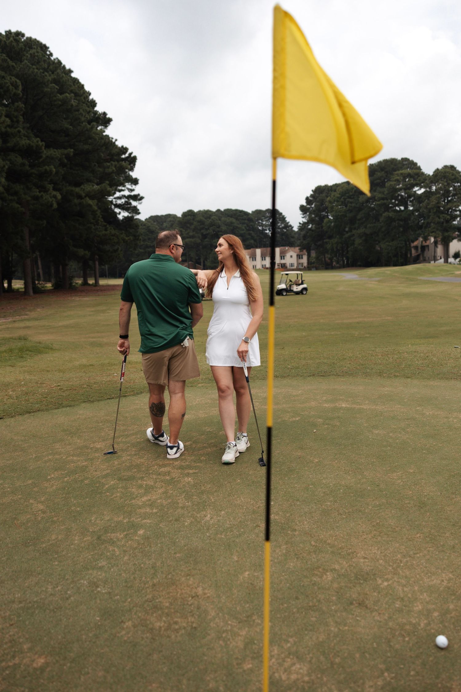 Couple sharing a joyful moment on a golf course green with a yellow flag in the foreground.