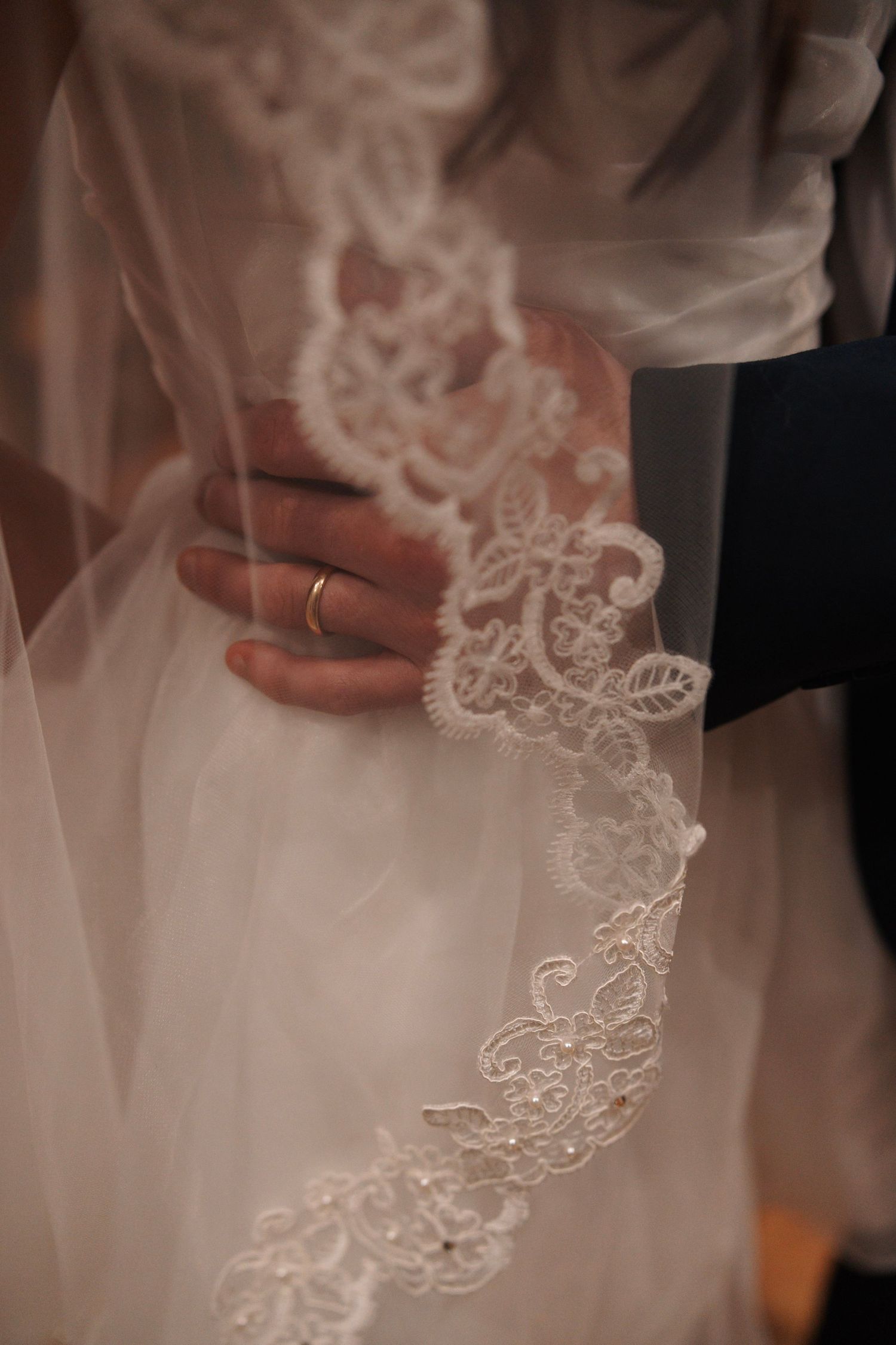 Close-up of bride and groom embracing, showcasing intricate lace wedding veil detail.