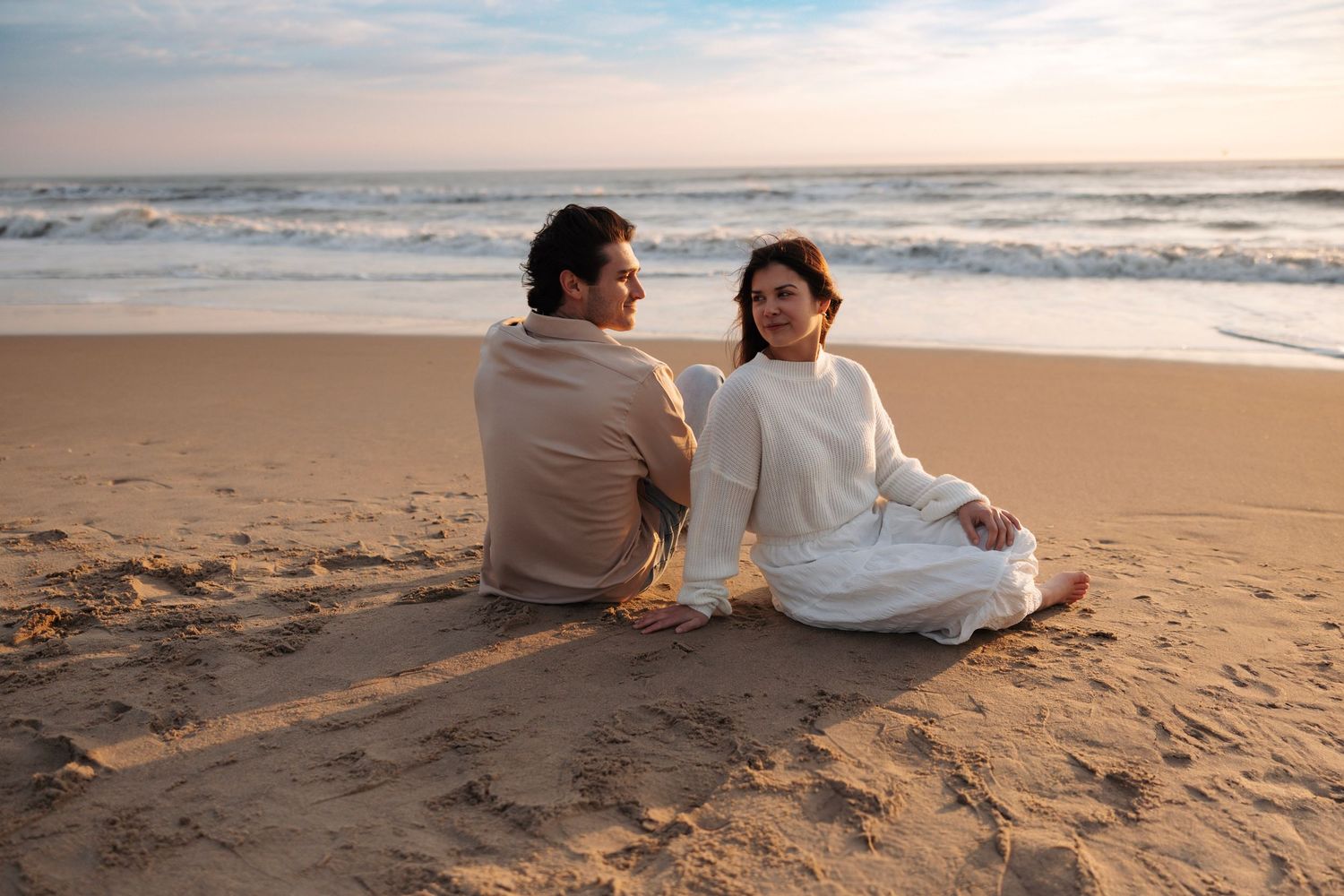 Couple sitting together on sandy beach at sunset sharing a romantic moment.