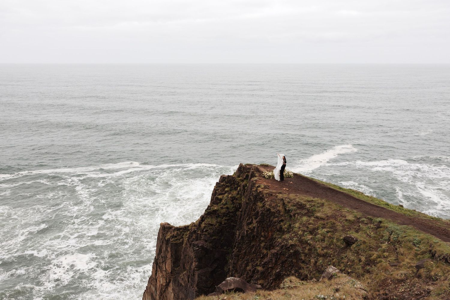 Solitary figure standing on rugged ocean cliff edge overlooking vast stormy Pacific coastline.