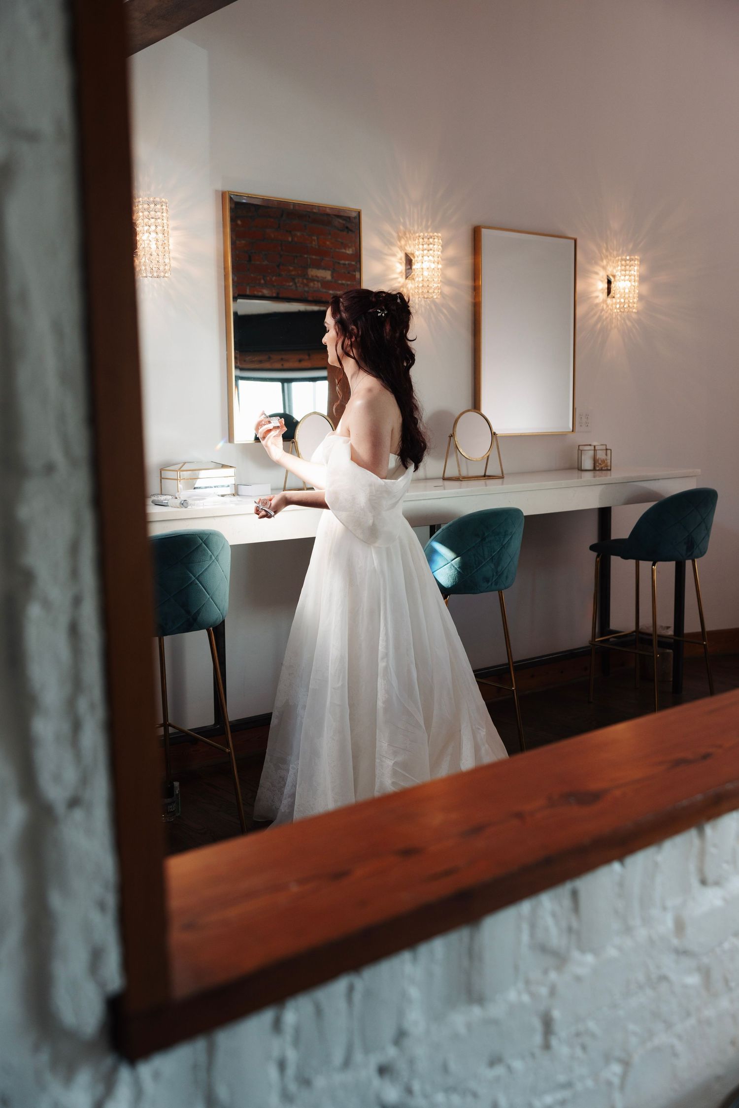 Elegant bride in off-shoulder white ballgown viewed through mirror reflection at a vanity dressing table.