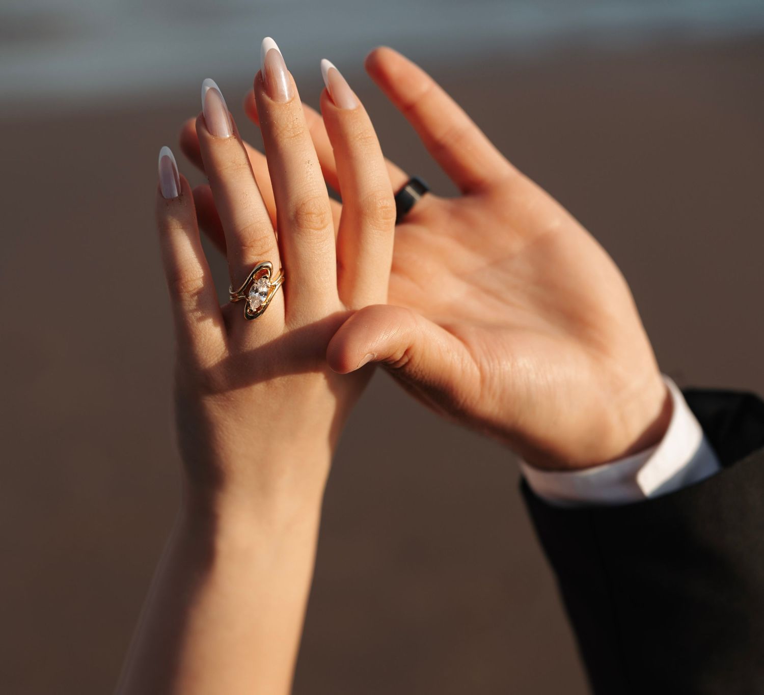 Close-up of hands showing a gold engagement ring being placed on a finger at the beach.