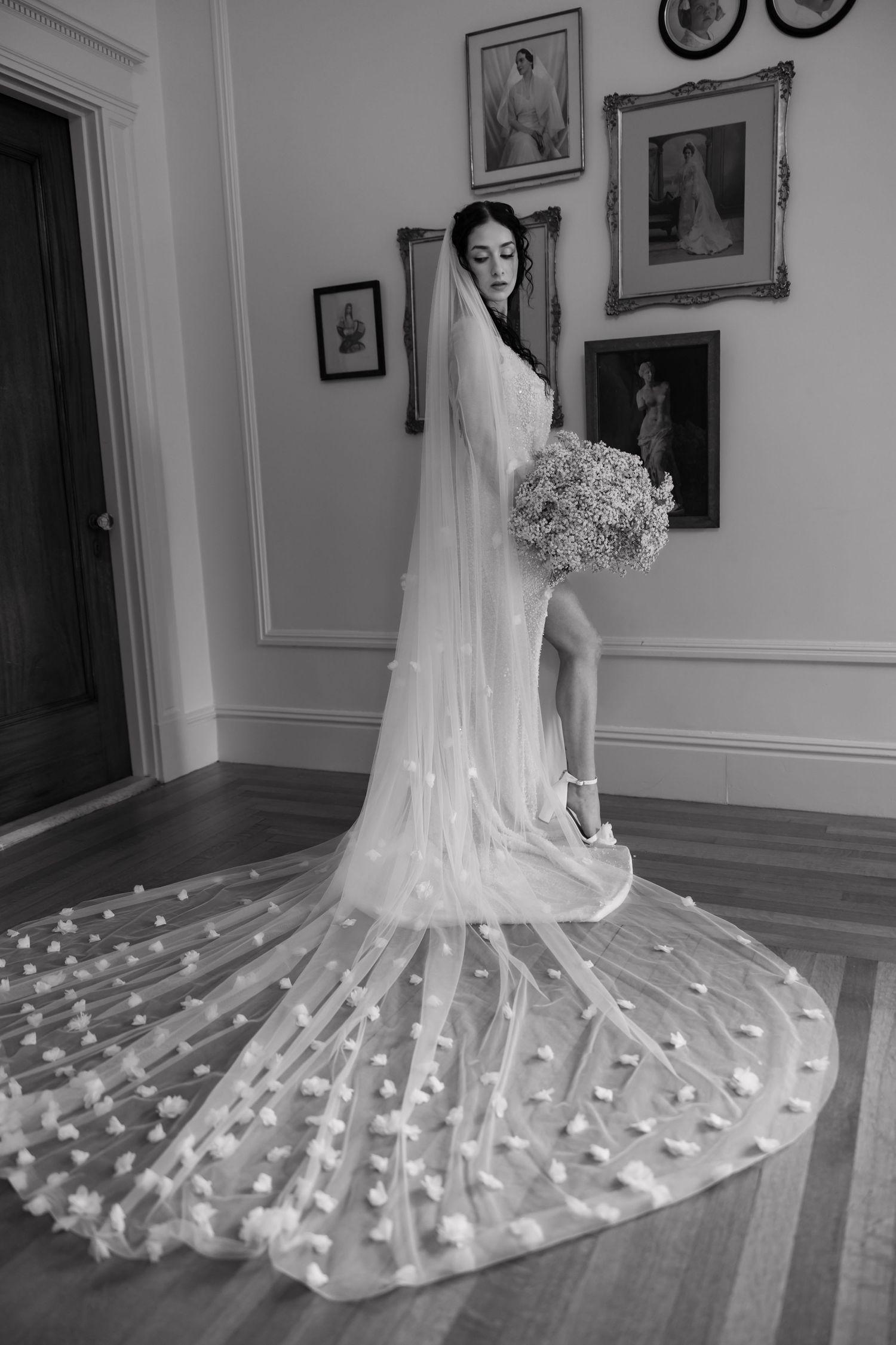 Bride in stunning wedding gown with long floral cathedral veil poses in black and white portrait.